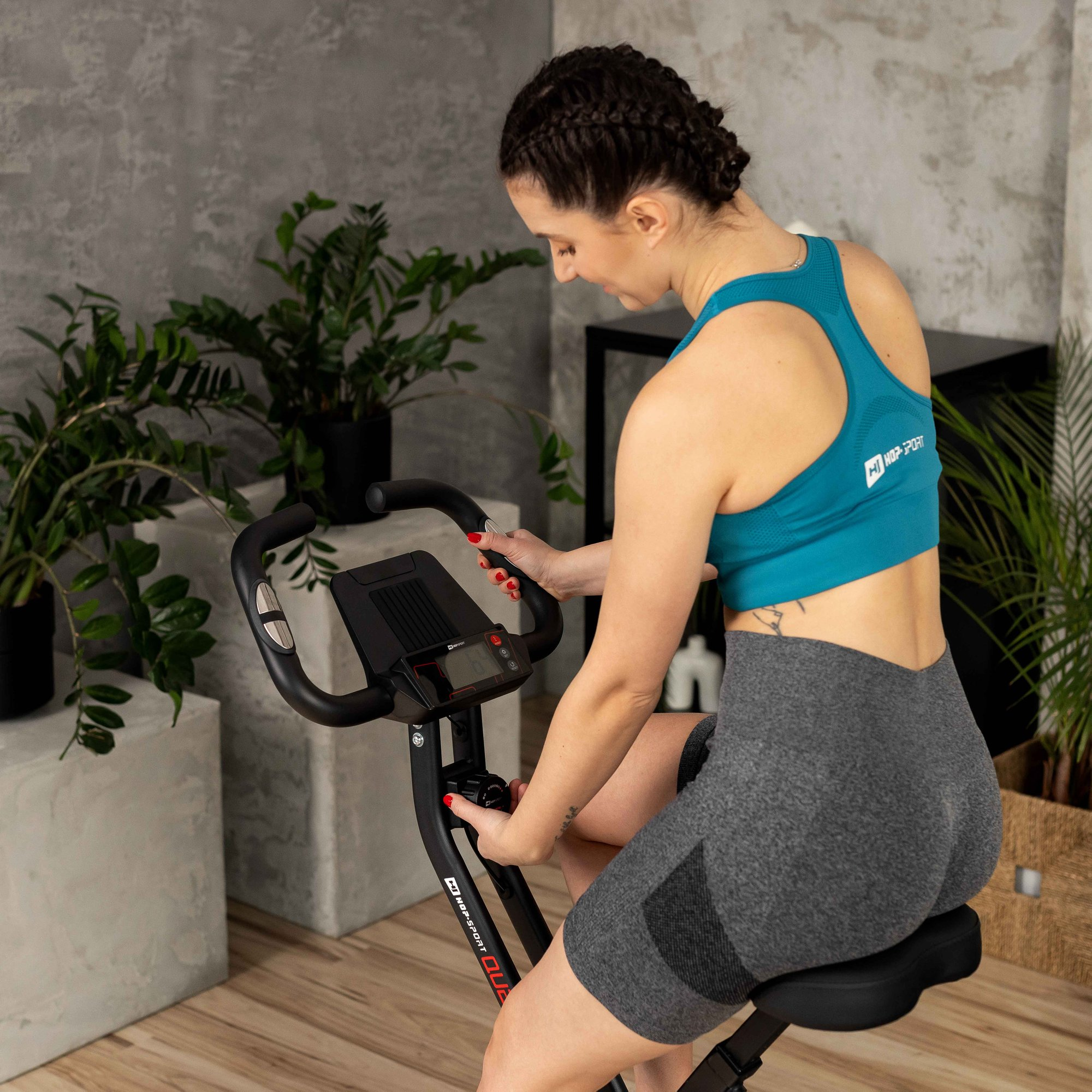 Eine Frau in Sportkleidung sitzt drinnen auf einem Heimtrainer.
