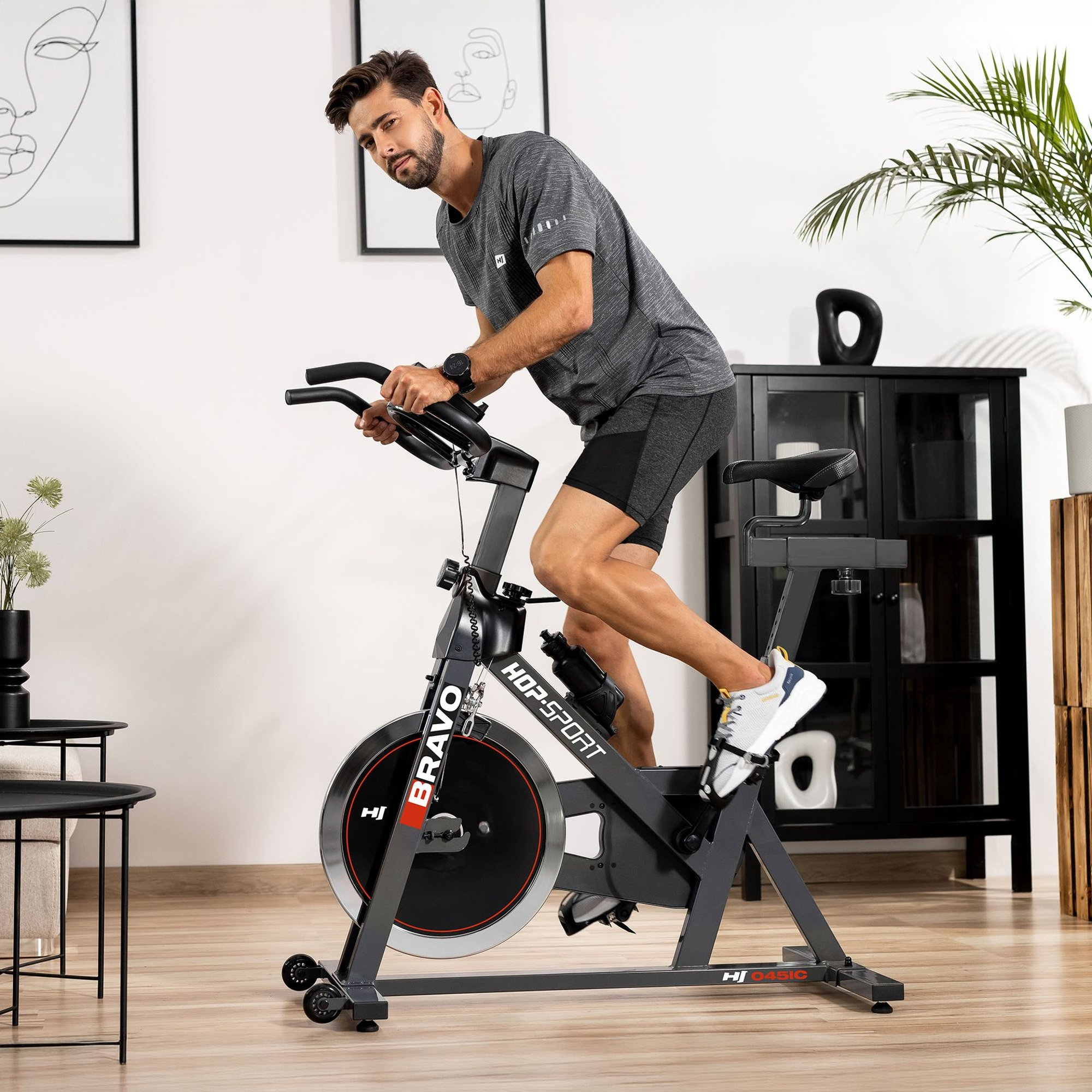 Ein Mann in grauer Sportkleidung fährt in einem modernen Zimmer auf einem Heimtrainer.