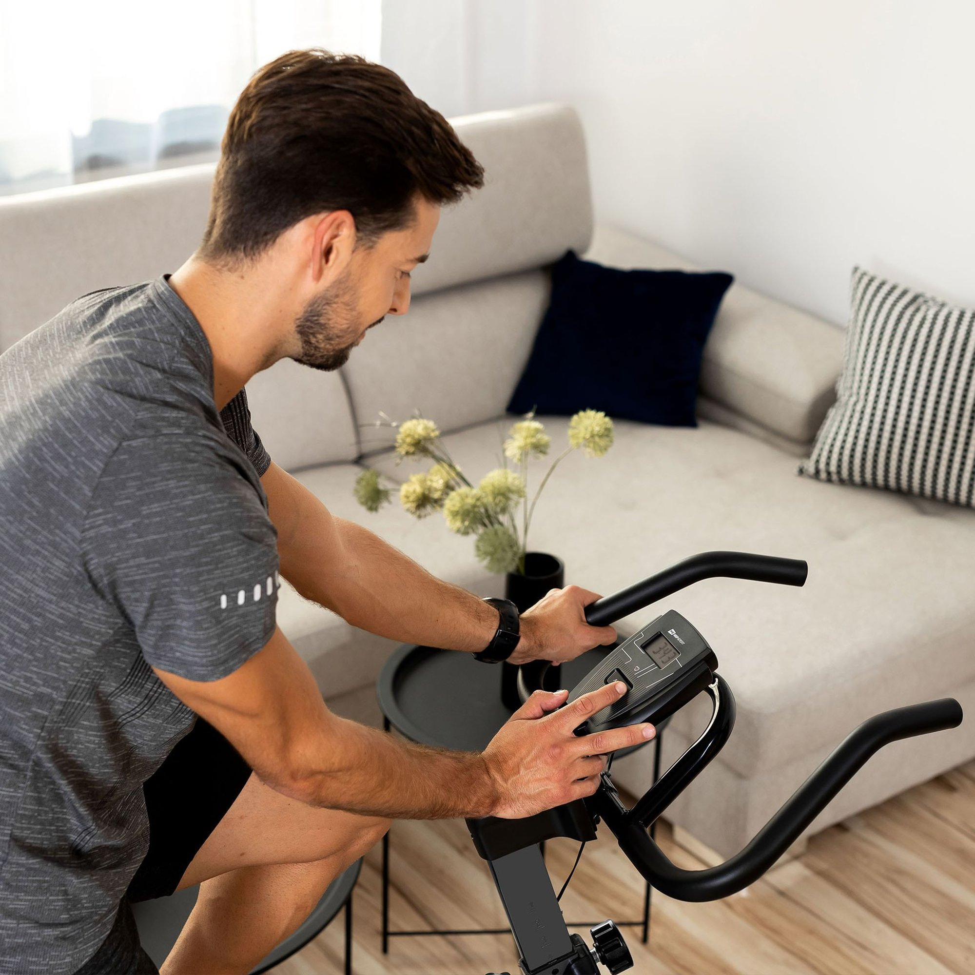 Ein Mann in Sportkleidung trainiert zu Hause auf einem Heimtrainer vor einem Sofa.