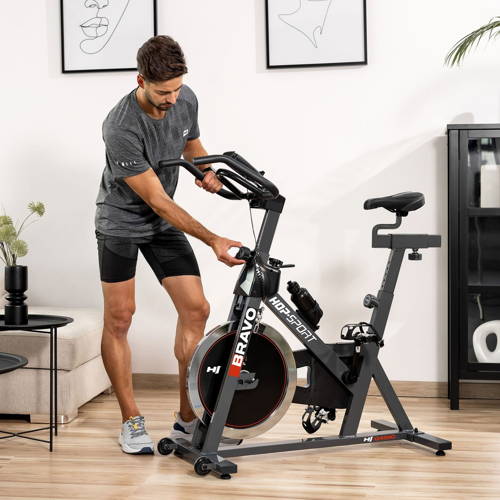 Ein Mann in Sportkleidung stellt den Widerstand eines grauen Heimtrainers in einem hellen Zimmer ein.
