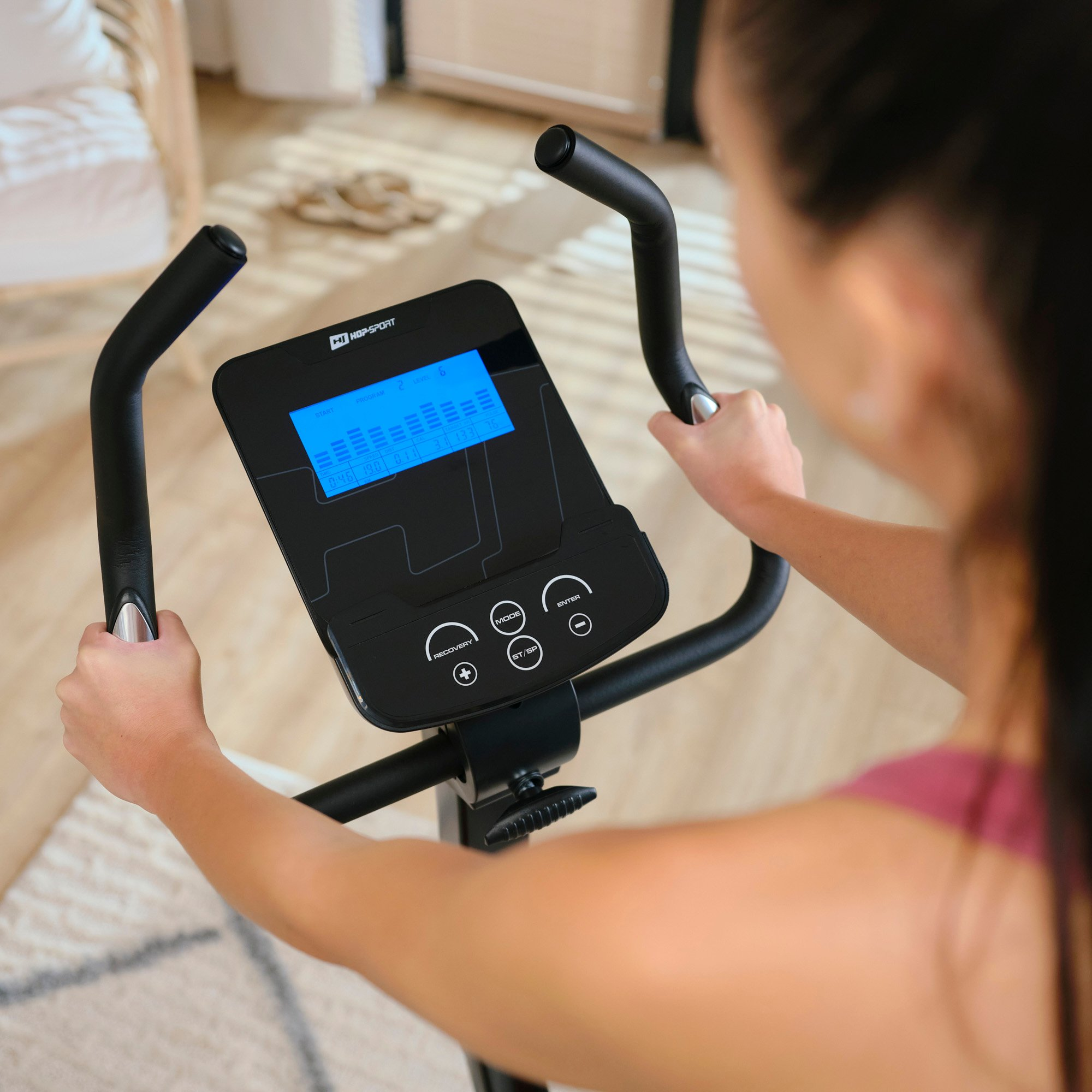 Eine Frau sitzt auf einem Heimtrainer und hält die Griffe mit einem blauen Display fest.