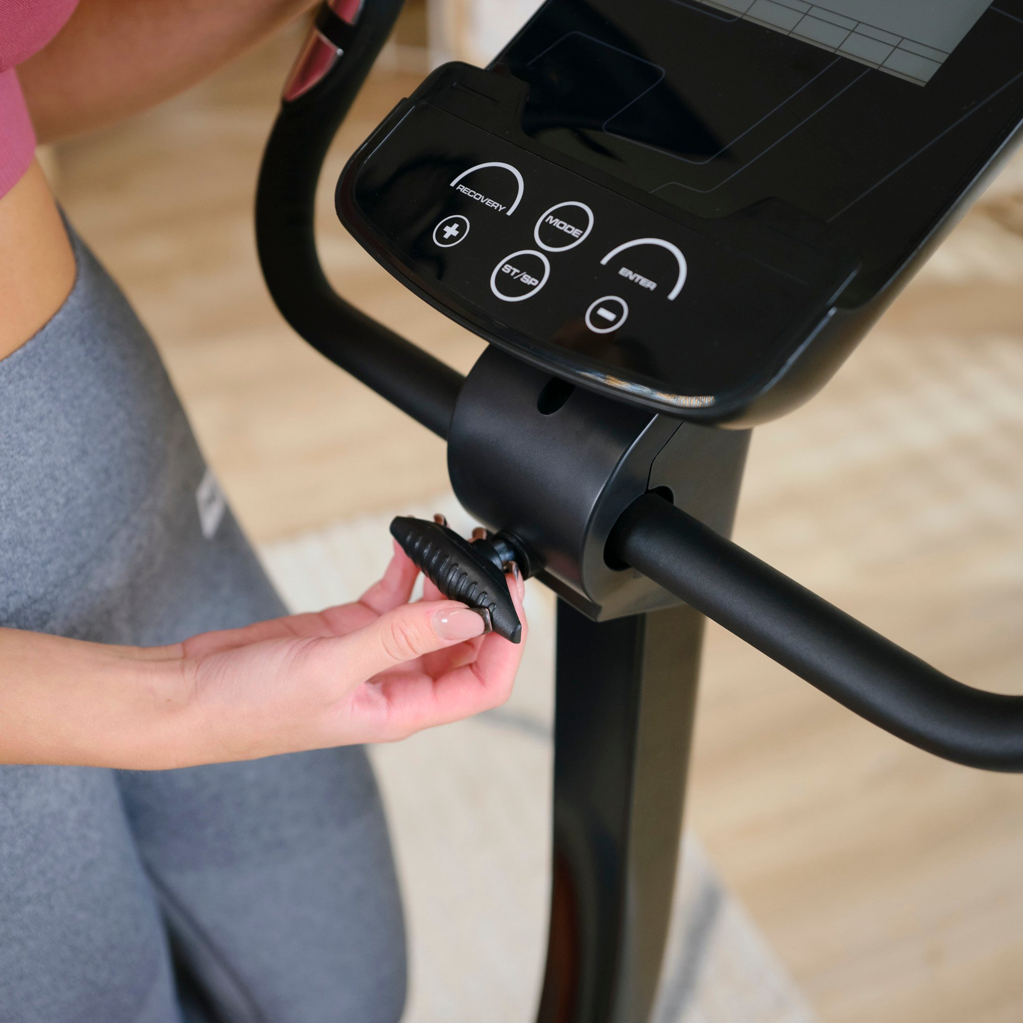 Eine Frau in Sportkleidung stellt den Widerstand an einem schwarzen Crosstrainer ein.