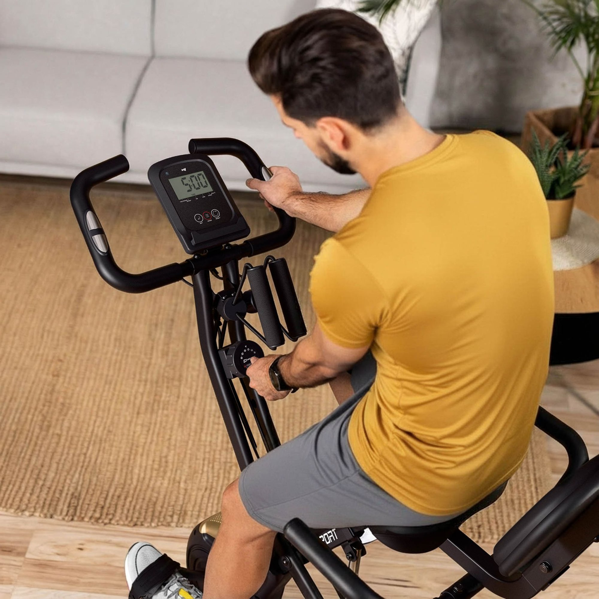 Ein Mann im gelben Shirt trainiert zu Hause auf einem schwarzen Heimtrainer.
