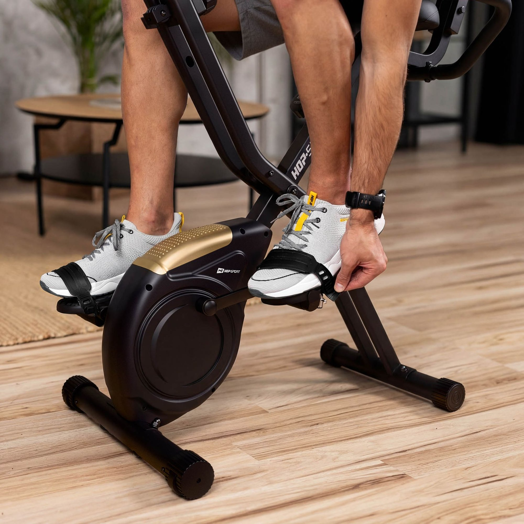 Eine Person sitzt auf einem Heimtrainer auf Holzfußboden und befestigt die Fußriemen.