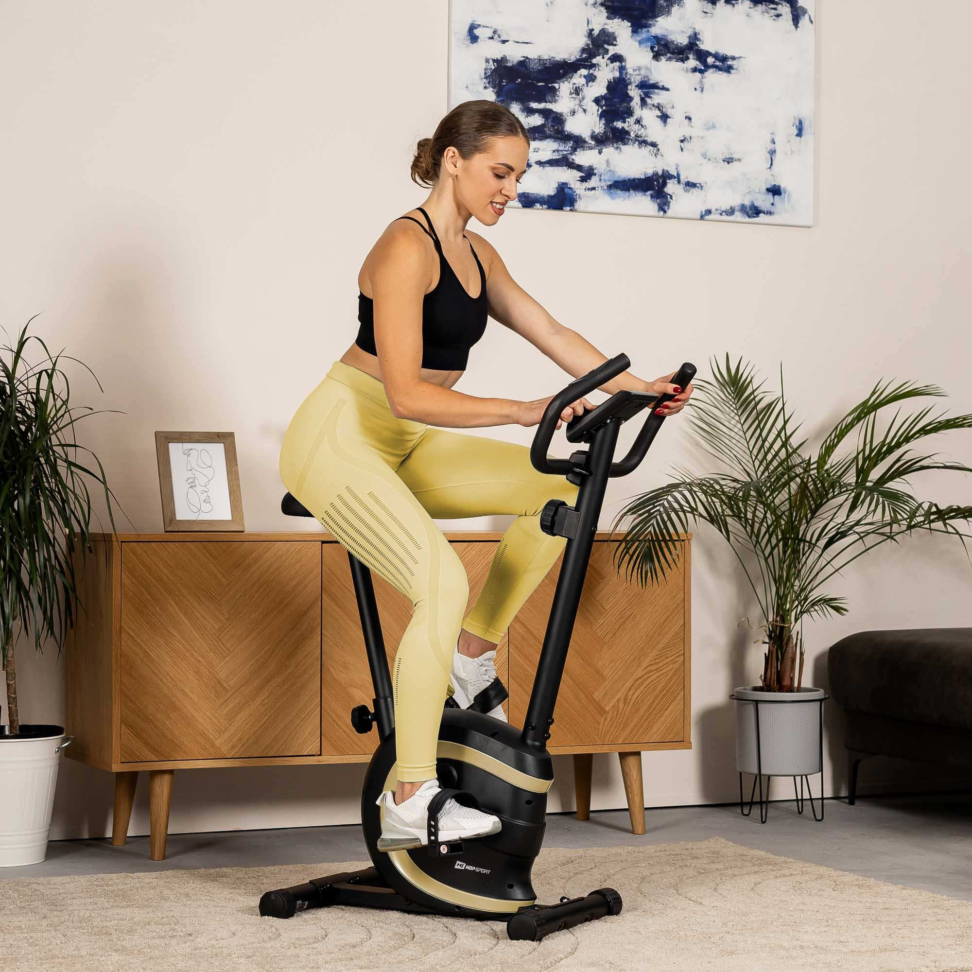 Eine Frau in Sportkleidung trainiert zu Hause auf einem Heimtrainer.