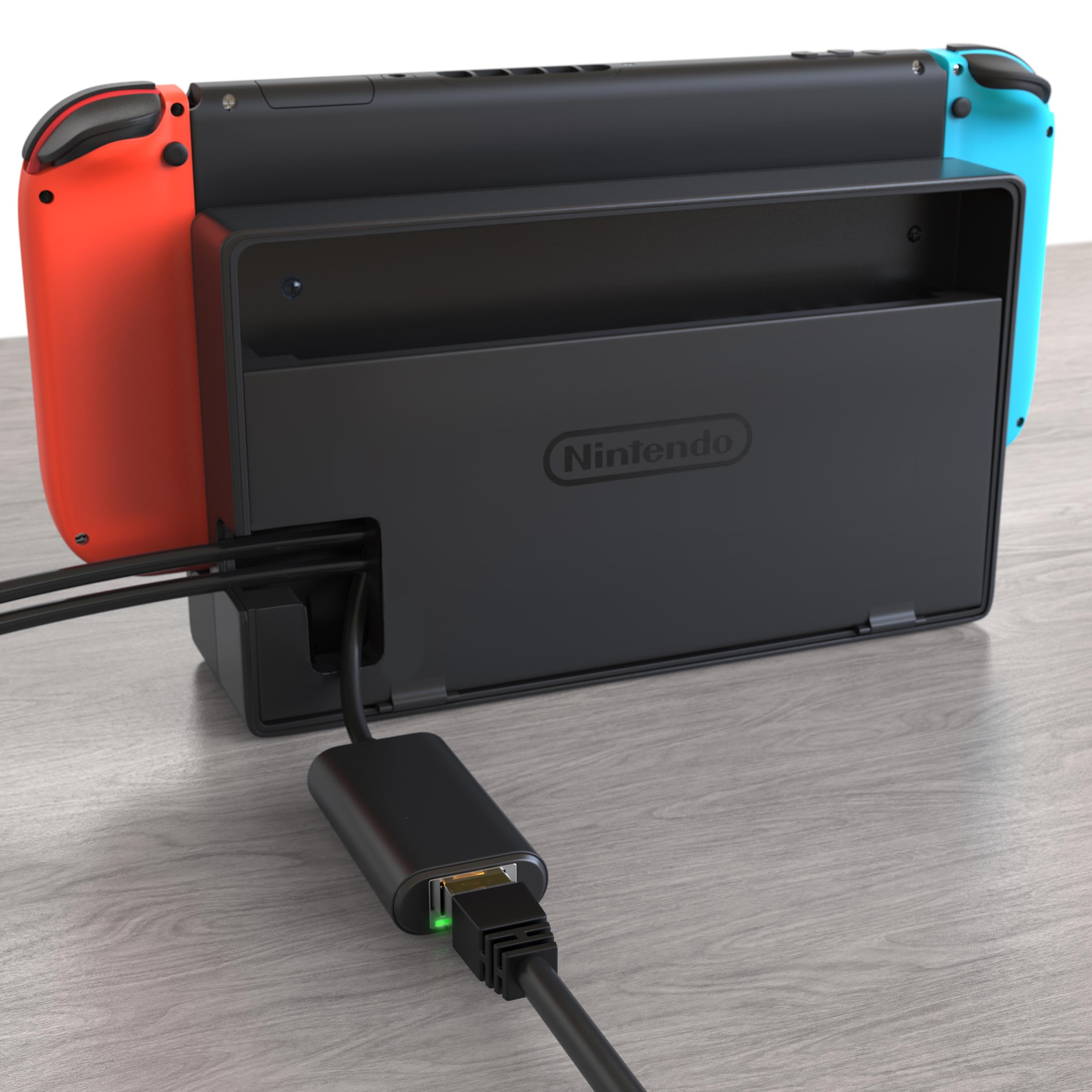 Eine Nintendo Switch Konsole in der Dockingstation mit angeschlossenem Ethernet-Adapter auf einem Holztisch.