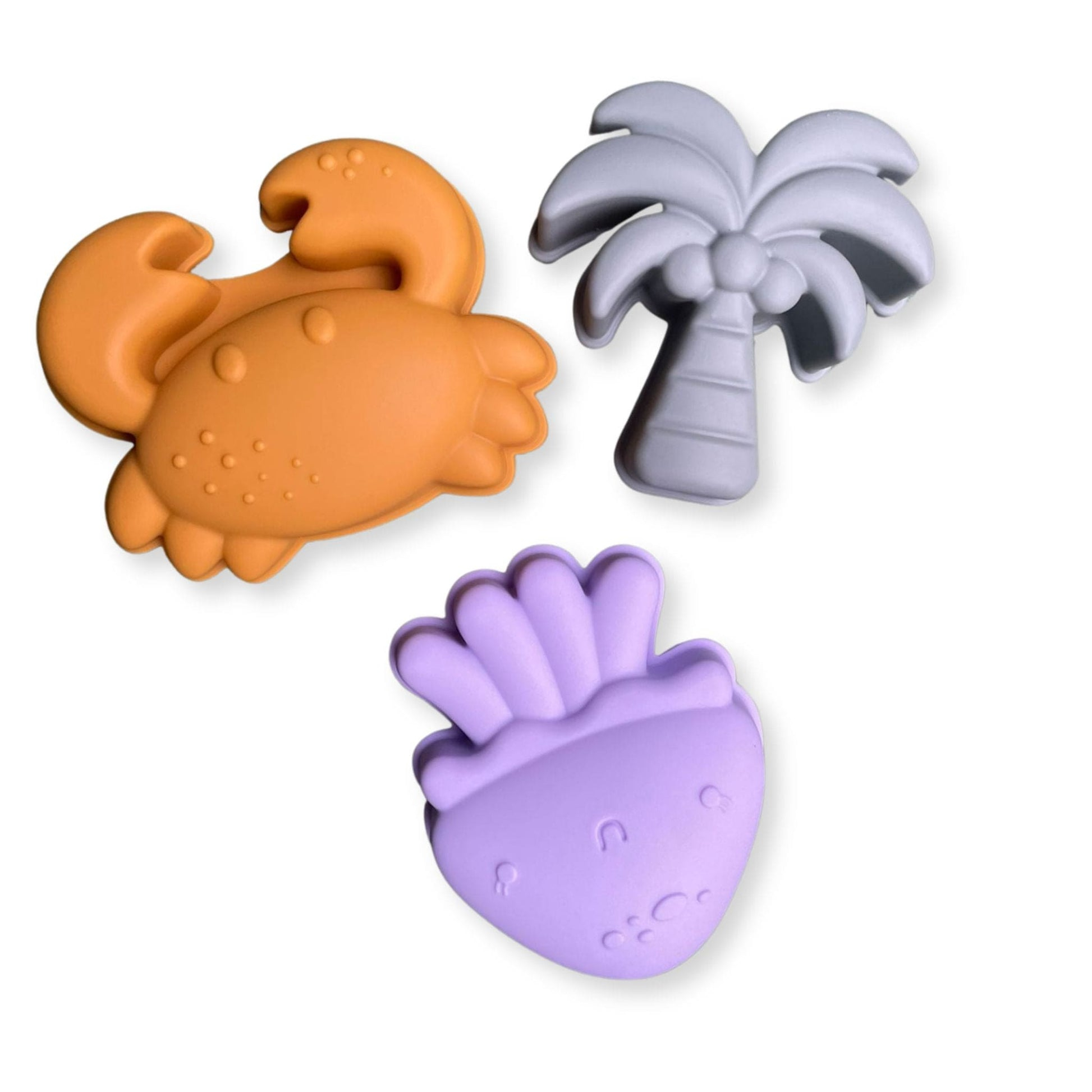 Tres moldes de silicona para arena con forma de cangrejo, palmera y baya sobre fondo blanco.
