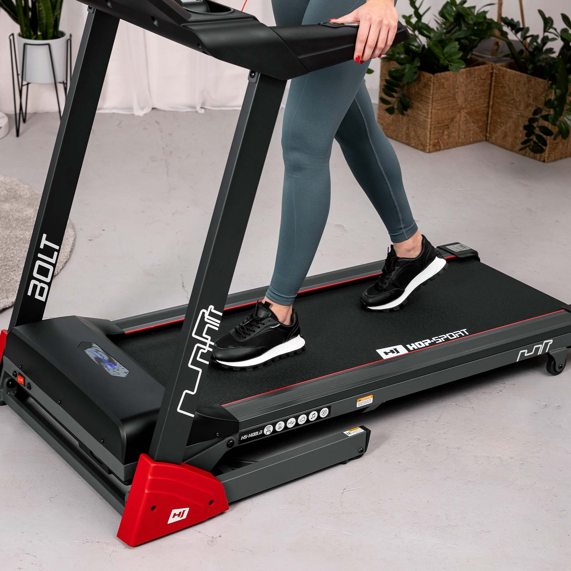 Eine Frau läuft in blauen Leggings und schwarzen Sneakers auf einem schwarzen Laufband.