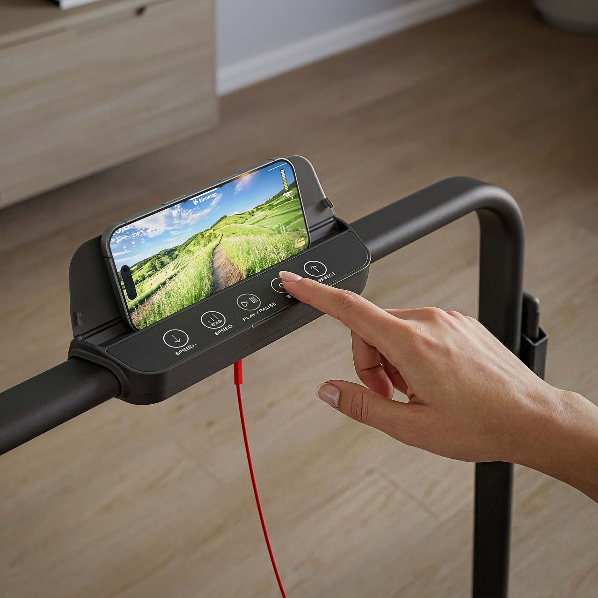 Eine Hand drückt einen Knopf auf einem Laufband mit Smartphone in der Halterung.