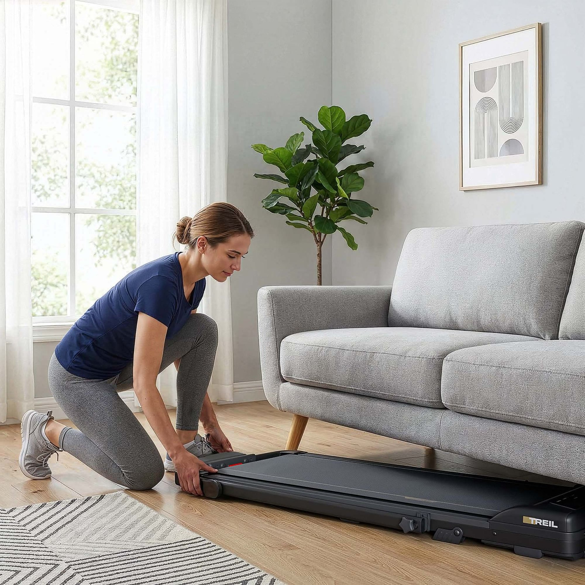 Eine Frau in Sportkleidung verstaut ein flaches Laufband unter einem grauen Sofa im Wohnzimmer.