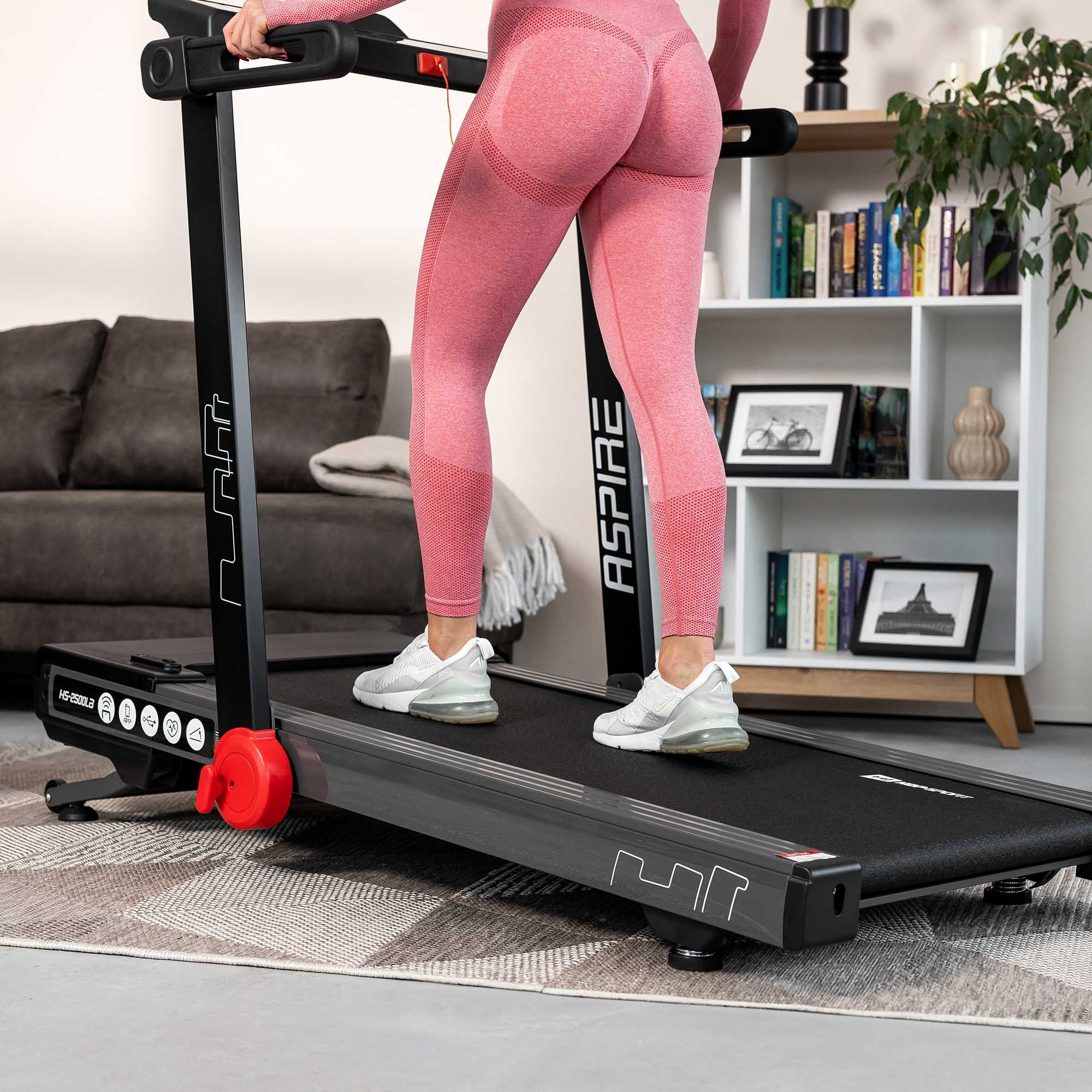 Eine Frau in rosa Sportbekleidung und weißen Turnschuhen geht auf einem schwarzen Laufband.