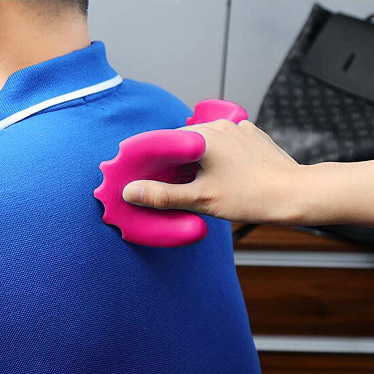 Eine Hand massiert den Rücken einer Person in einem blauen Hemd mit einem pinken Massagegerät.