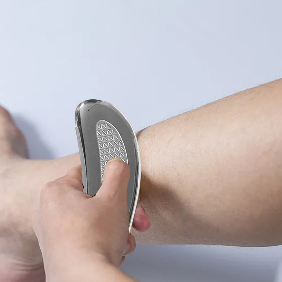 Eine Hand massiert ein menschliches Bein mit einem silbernen Gua Sha Metallwerkzeug.