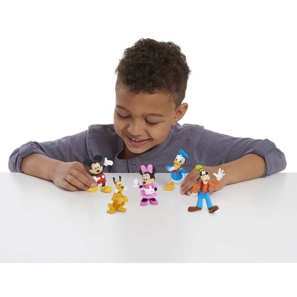 Ein Junge in einem grauen Hemd spielt mit Disney-Figuren auf einem weißen Tisch.