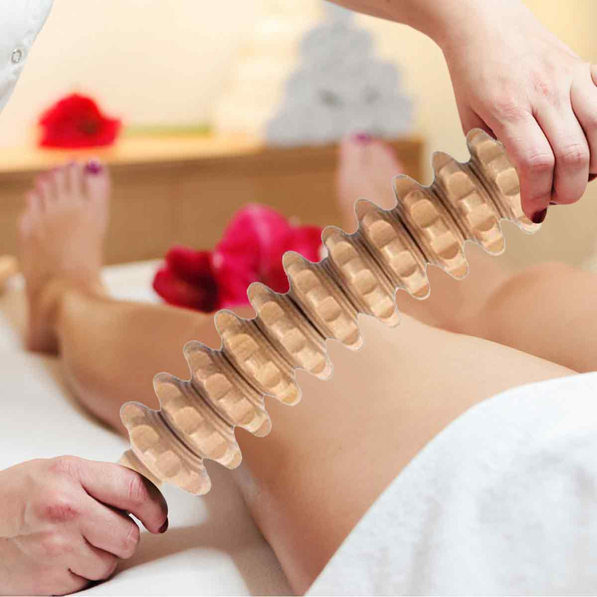 Eine Person massiert die Beine mit einer hölzernen Massagerolle auf einer Liege in einem Wellnessbereich.