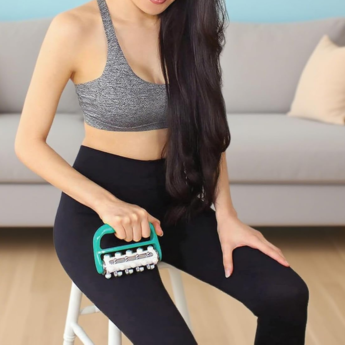 Frau in Sportkleidung nutzt einen grünen Handmassage-Roller am Oberschenkel.