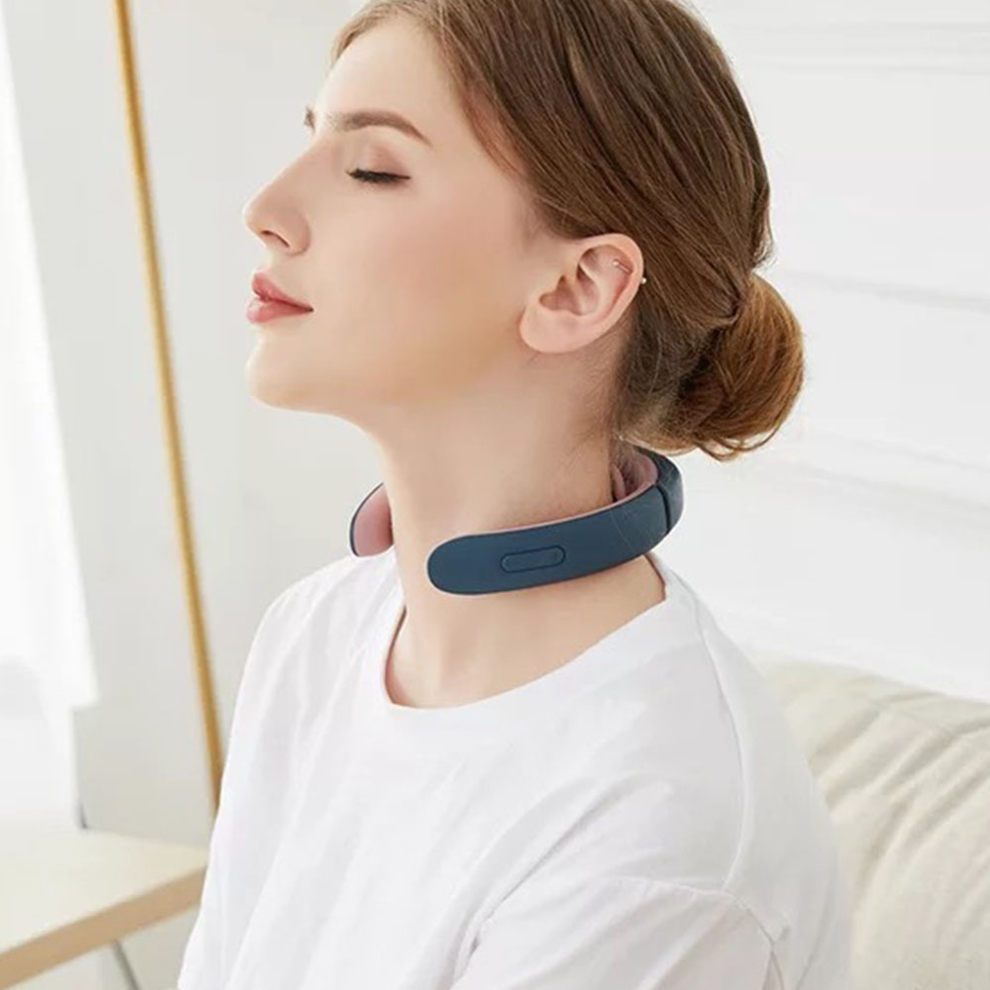 Eine Frau mit geschlossenen Augen trägt ein blaues Nackenmassagegerät in einem hellen Zimmer.