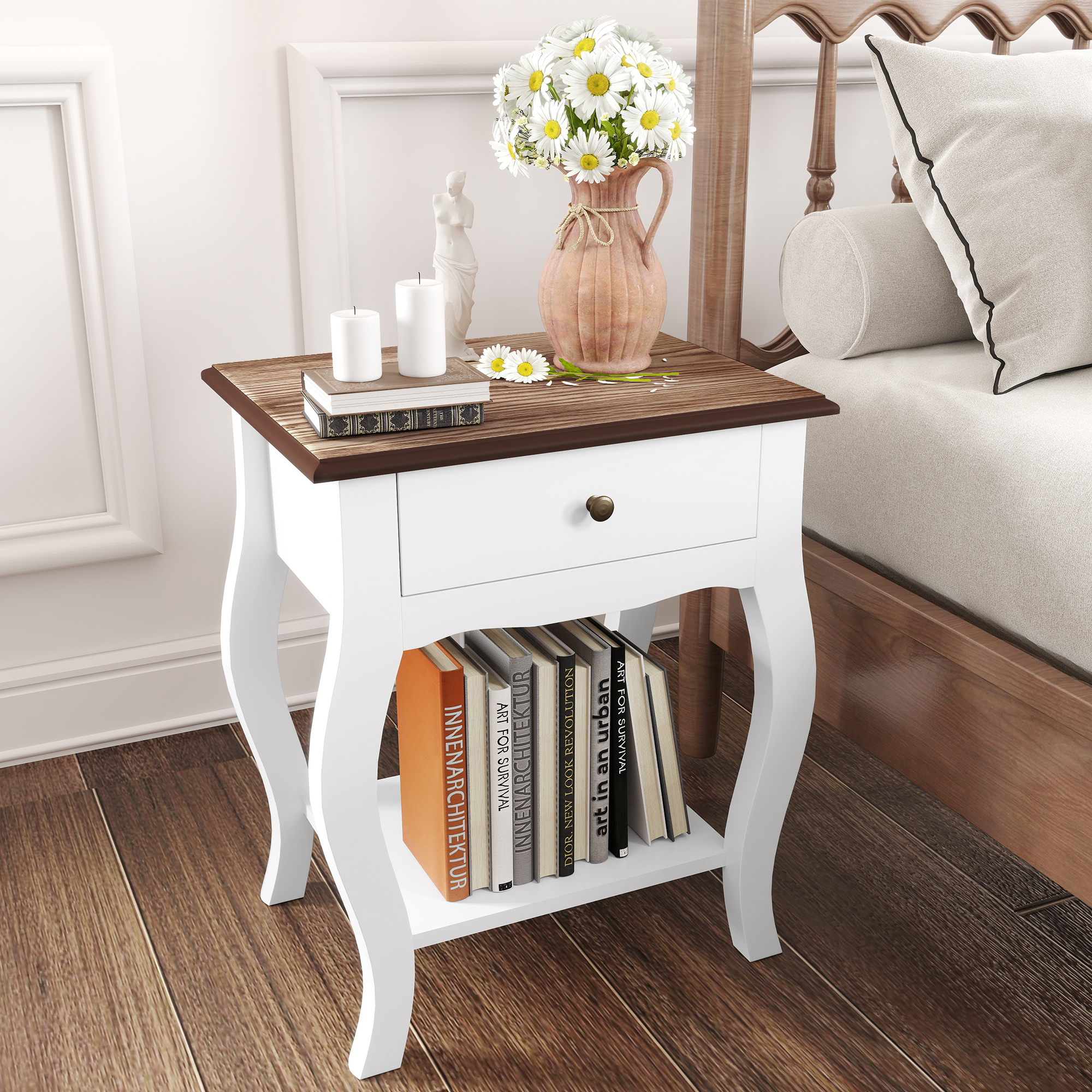 Mesita de noche blanca con tapa de madera oscura, flores, velas y libros al lado de una cama.