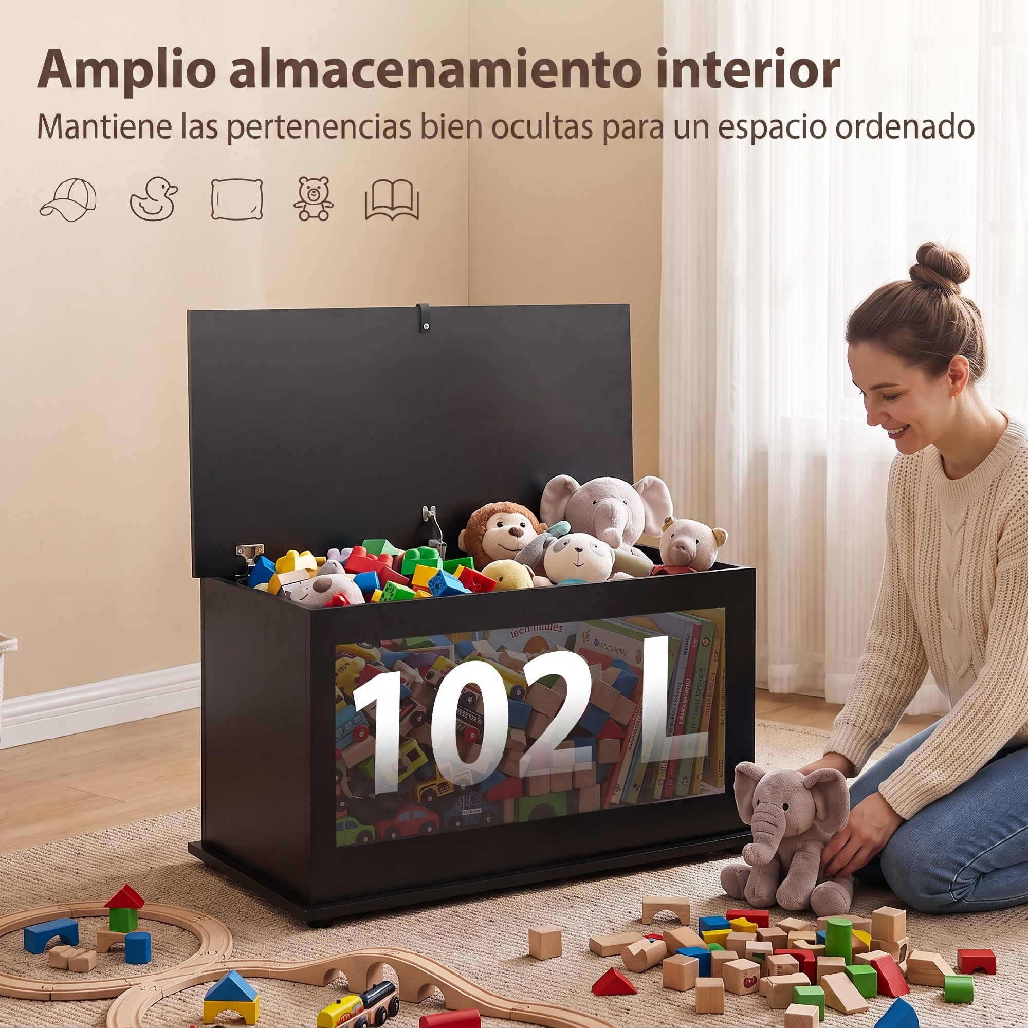 Una mujer se sienta junto a un gran baúl de juguetes negro lleno de peluches y bloques en una habitación luminosa.