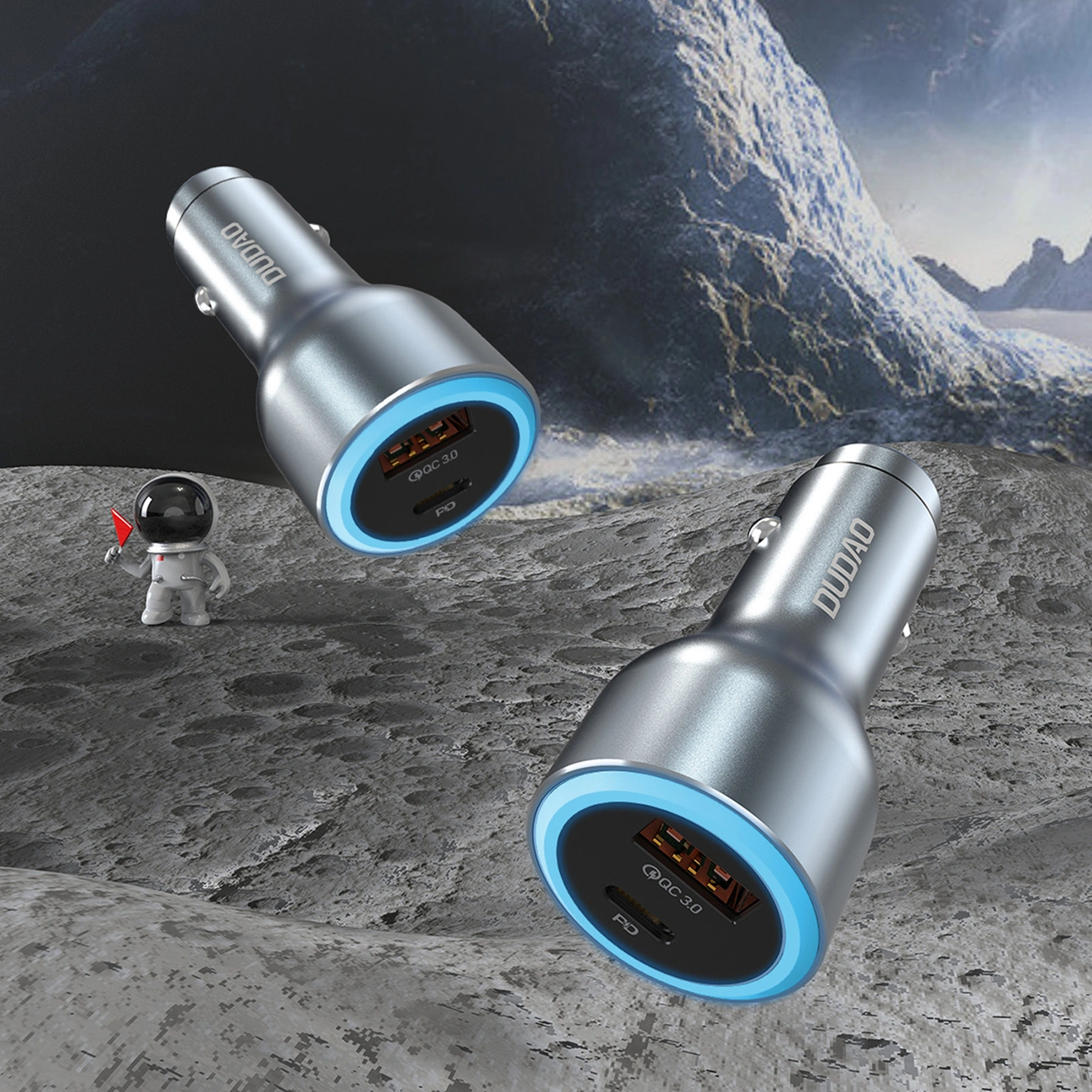Due caricabatterie USB argentati con luce ad anello blu fluttuano su un paesaggio lunare accanto a un piccolo astronauta.