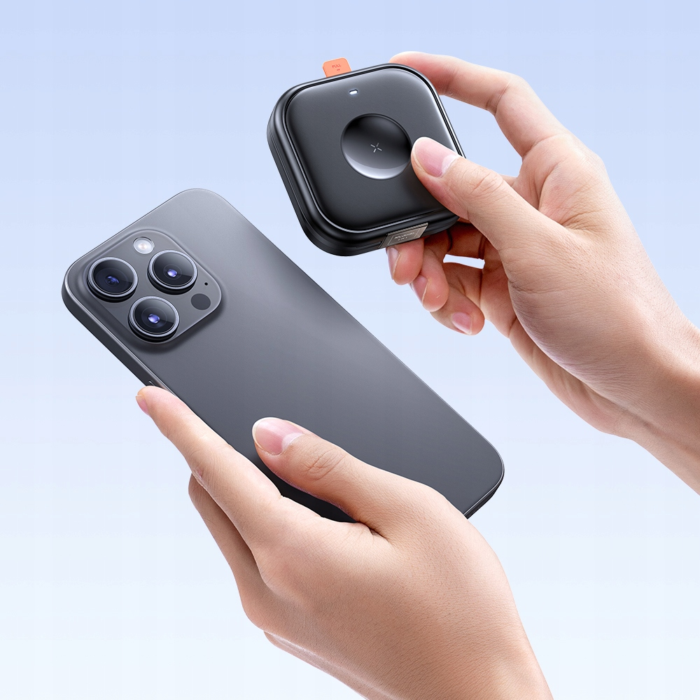 Una persona tiene in mano uno smartphone grigio e un piccolo power bank nero su sfondo azzurro.