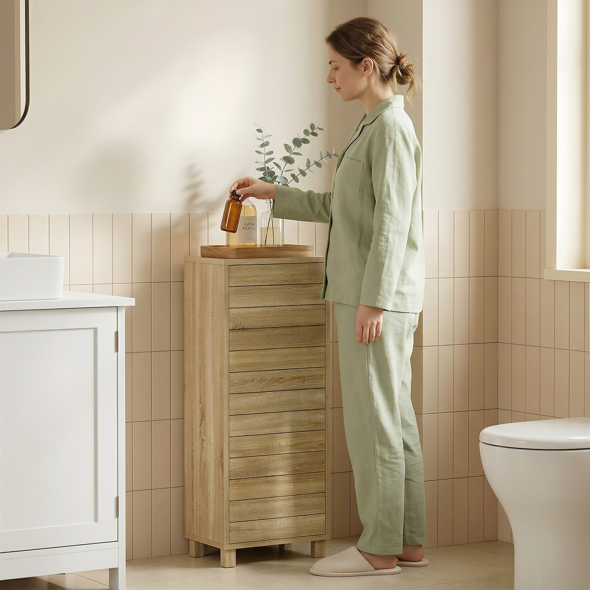 Una mujer en pijama verde coge un frasco sobre un mueble de madera en un baño luminoso.