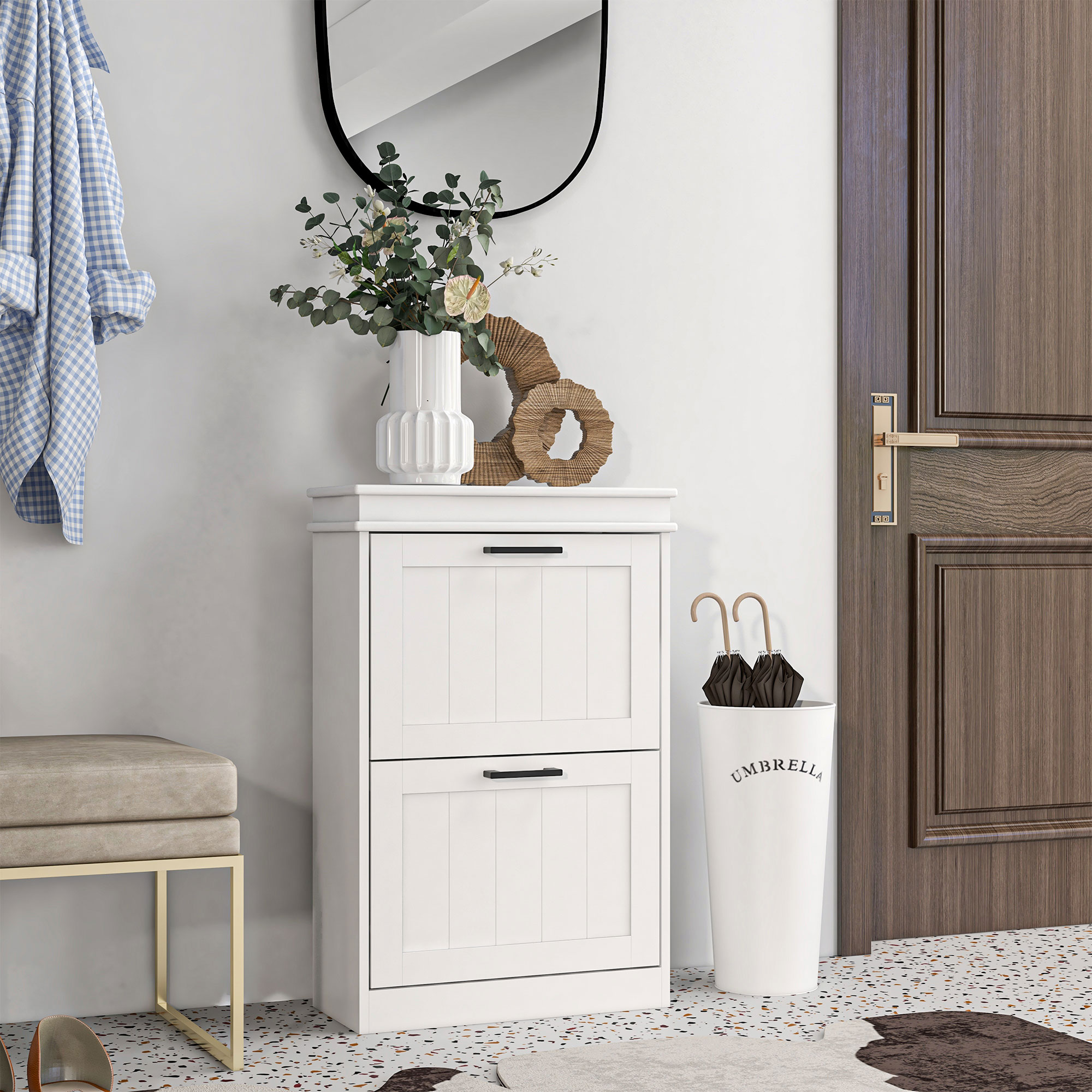 Un zapatero blanco en el pasillo con flores, un espejo redondo, paragüero y una puerta de madera oscura.