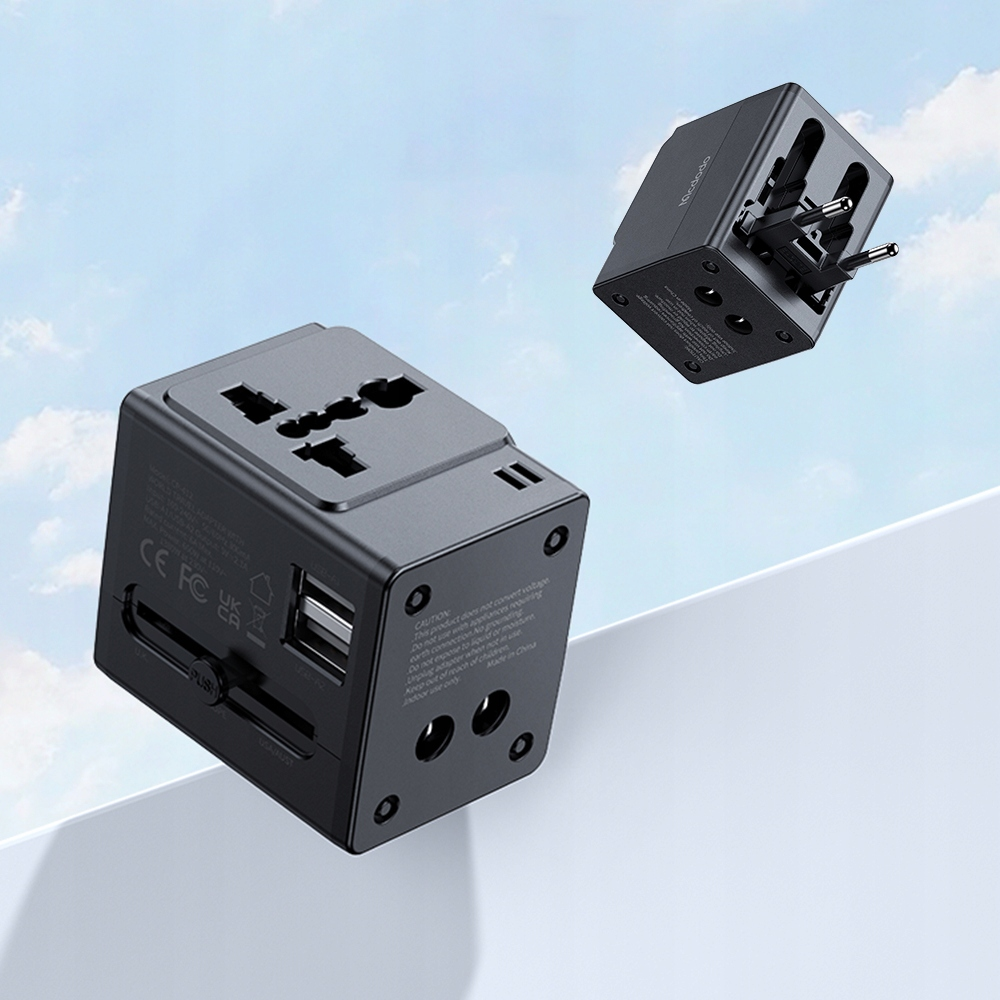 Due adattatori da viaggio universali neri fluttuano su un cielo azzurro con nuvole, mostrando porte USB e spine.