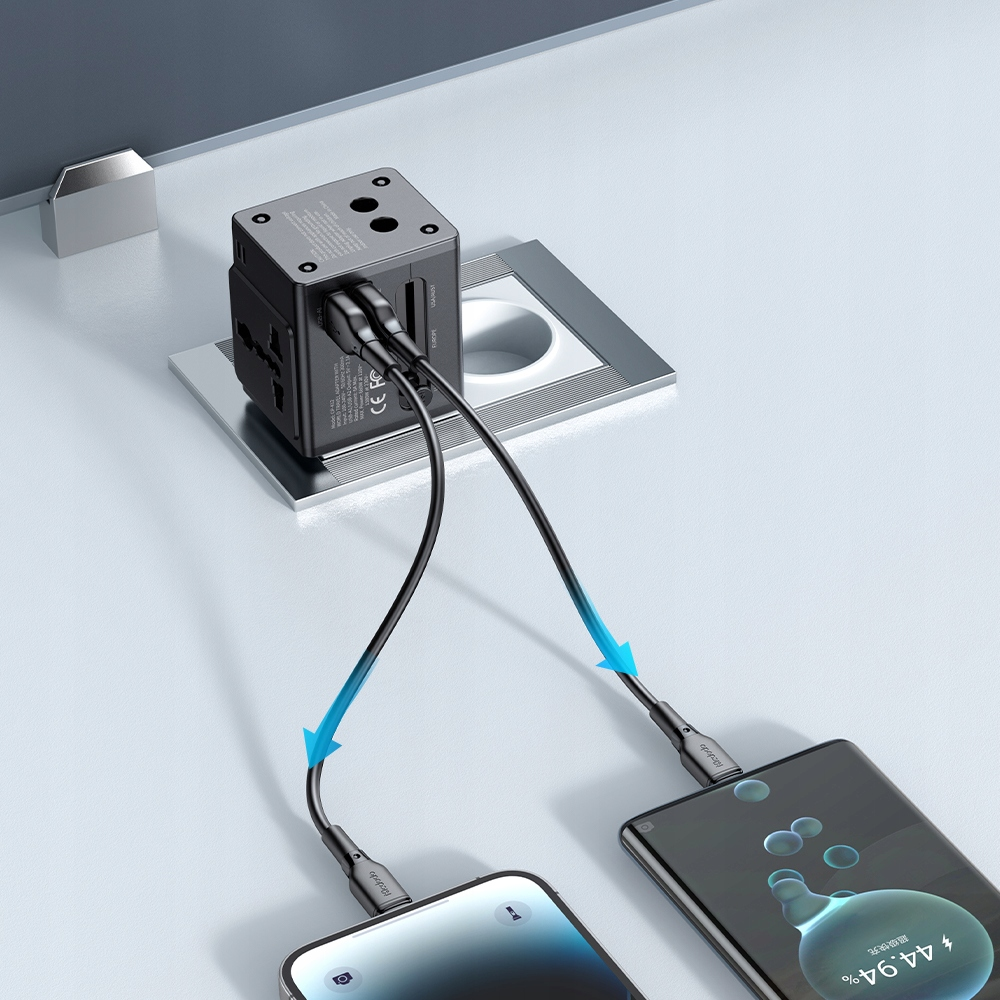 Un adattatore a muro grigio su una scrivania carica due smartphone con cavi neri e frecce blu.