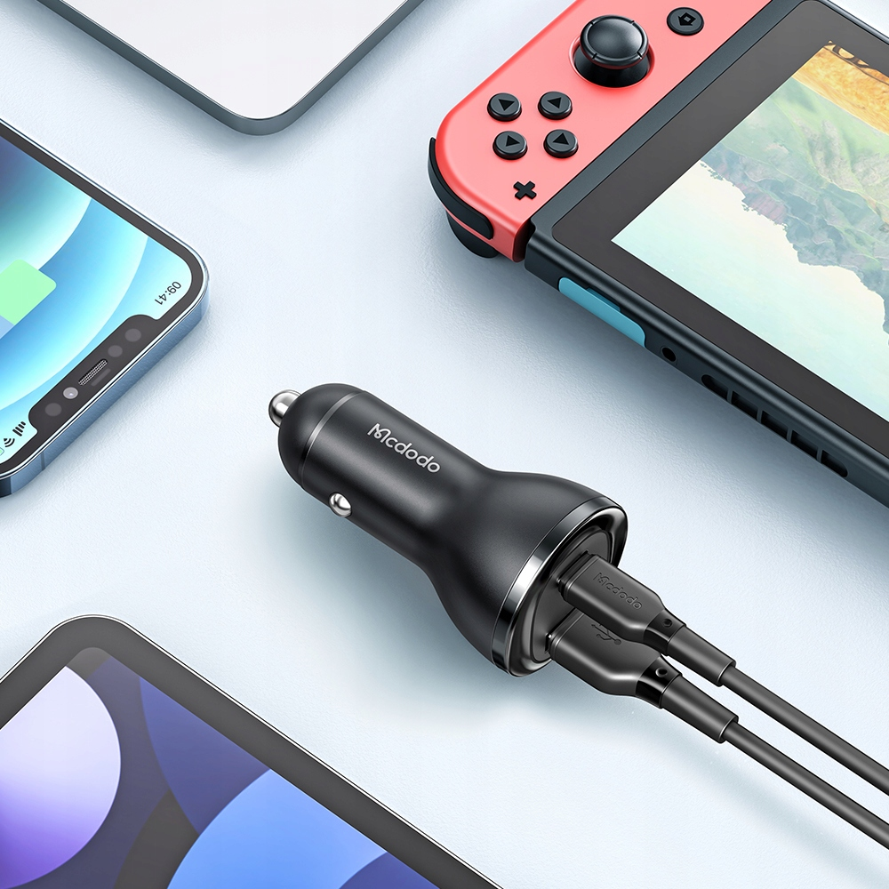 Un caricabatterie per auto Mcdodo nero con due cavi USB collegati, circondato da una Nintendo Switch e smartphone.
