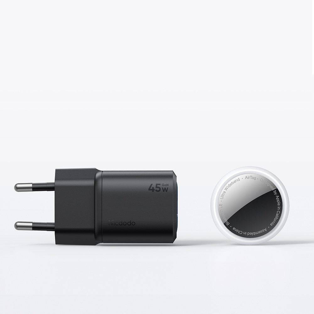 Beyaz bir zeminde AB fişli siyah 45W GaN duvar şarj cihazı ve yanında beyaz bir Apple AirTag.