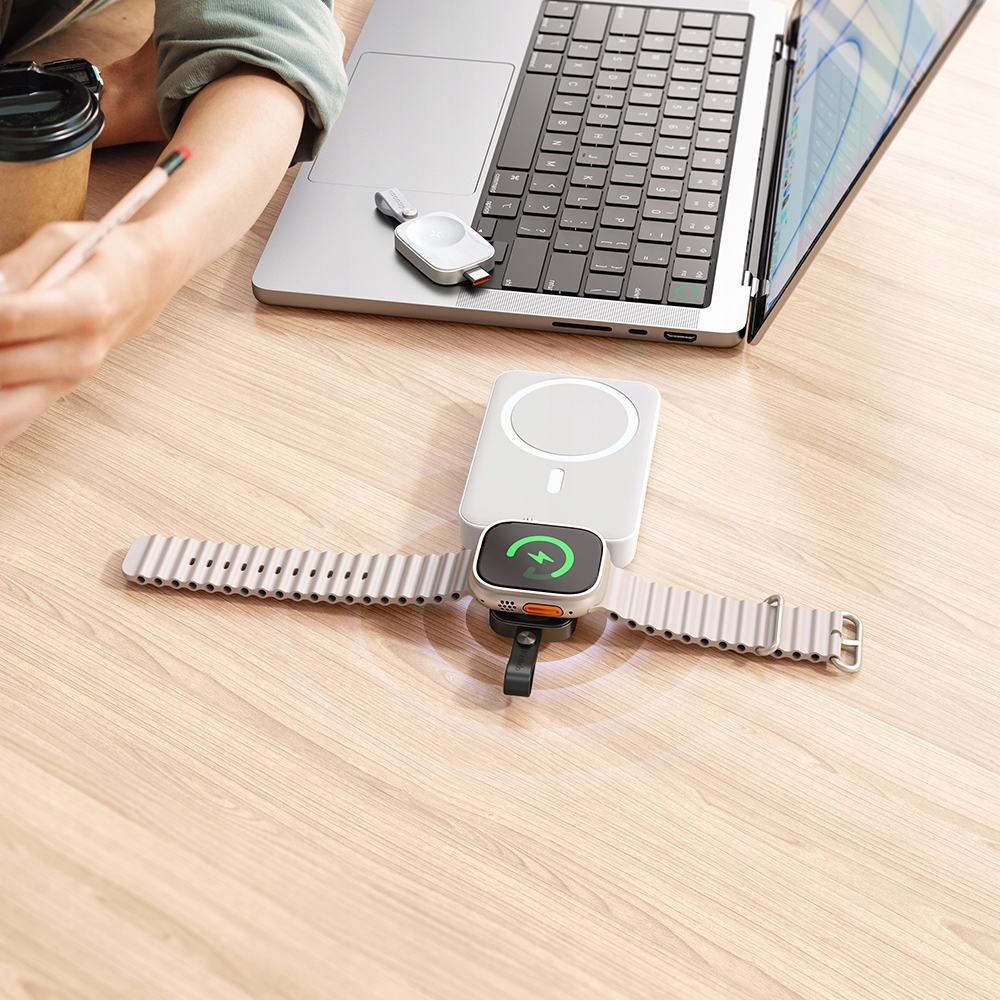 Uno smartwatch si ricarica in modalità wireless su una scrivania di legno accanto a un computer portatile.