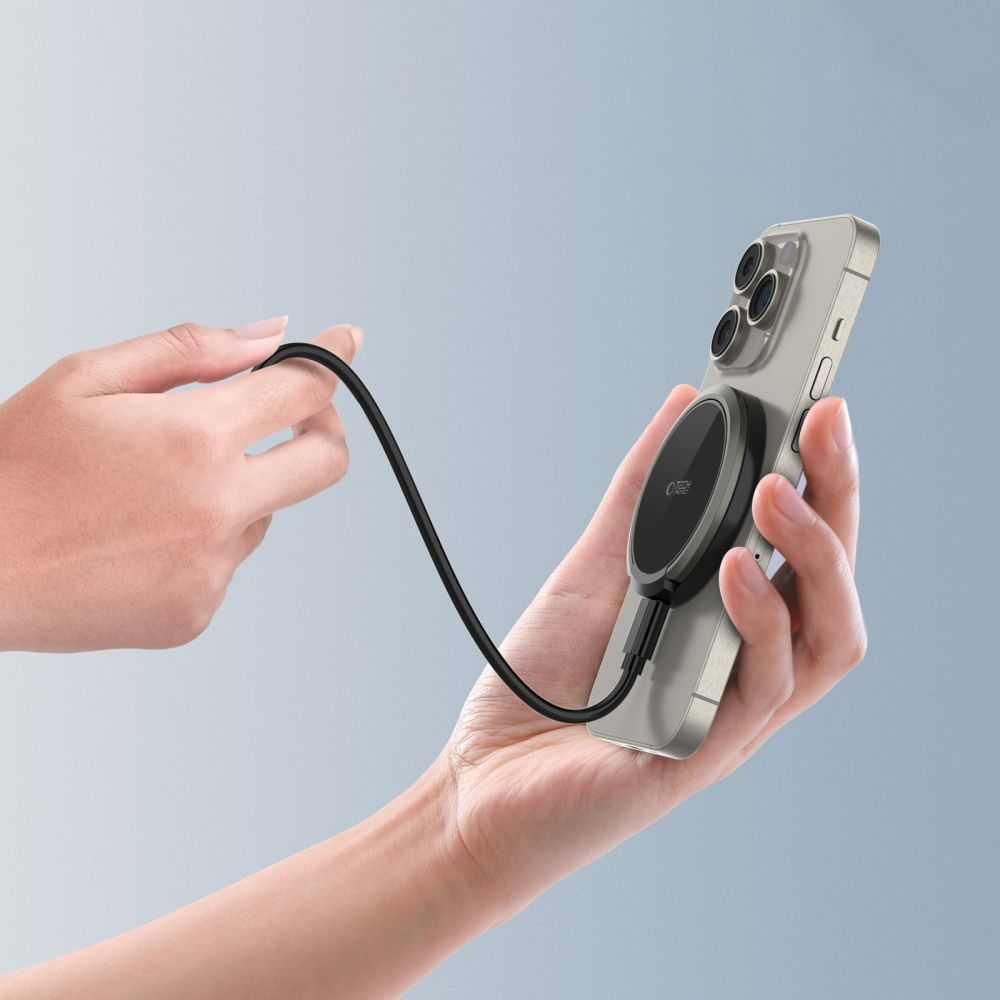 Una mano tiene uno smartphone con caricabatterie magnetico wireless sul retro, collegato da un cavo nero.