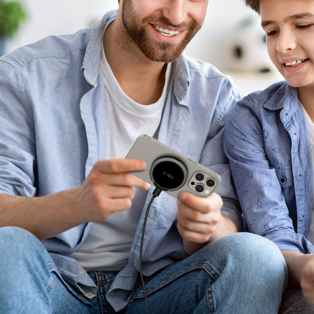 Un padre e suo figlio sorridono mentre il padre tiene in mano uno smartphone in carica.