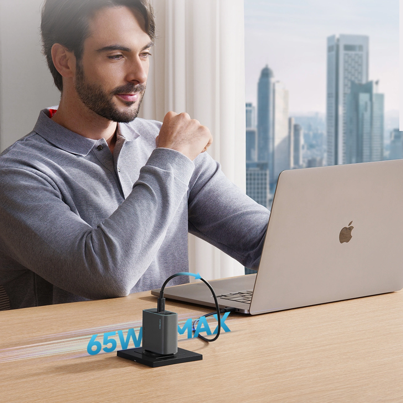 Ein Mann arbeitet an einem Laptop am Tisch, neben ihm ein 65W Max USB-Ladegerät.