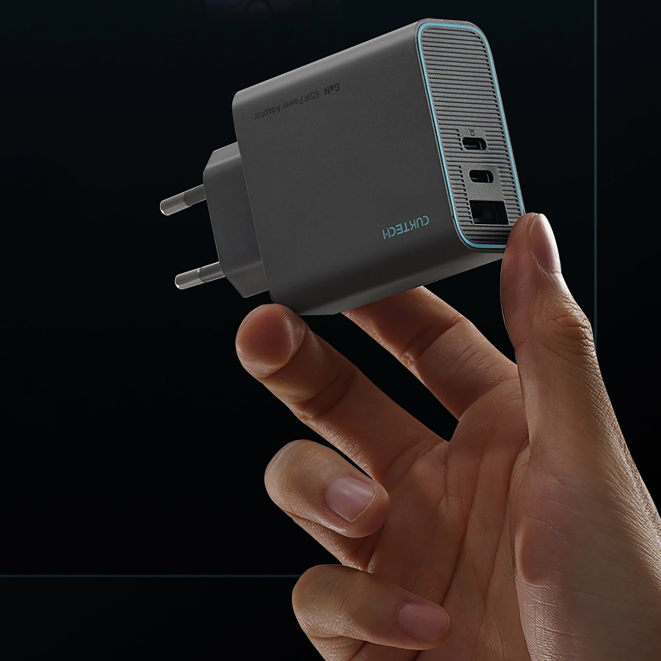 Eine Hand hält einen grauen Cuktech 65W GaN-Netzadapter mit USB-Ports vor dunklem Hintergrund.