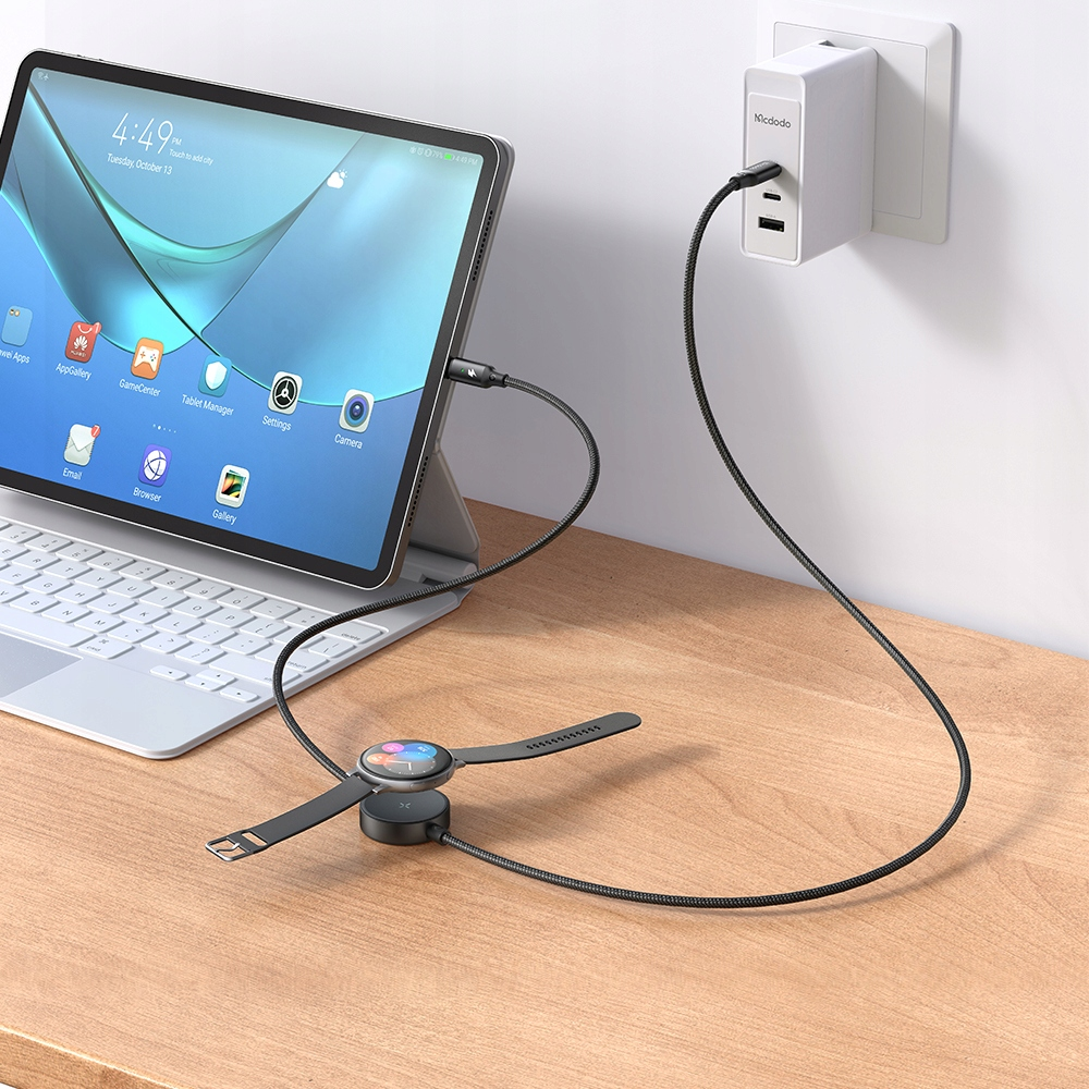 Un caricatore da muro bianco alimenta un tablet e uno smartwatch su una scrivania in legno.