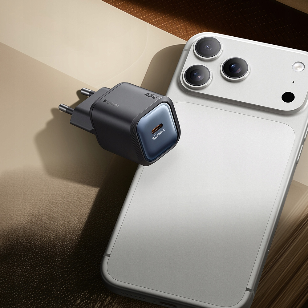 Açık kahverengi bir yüzeyde, gümüş renkli bir akıllı telefonun yanında gri bir 45W USB-C hızlı şarj cihazı duruyor.