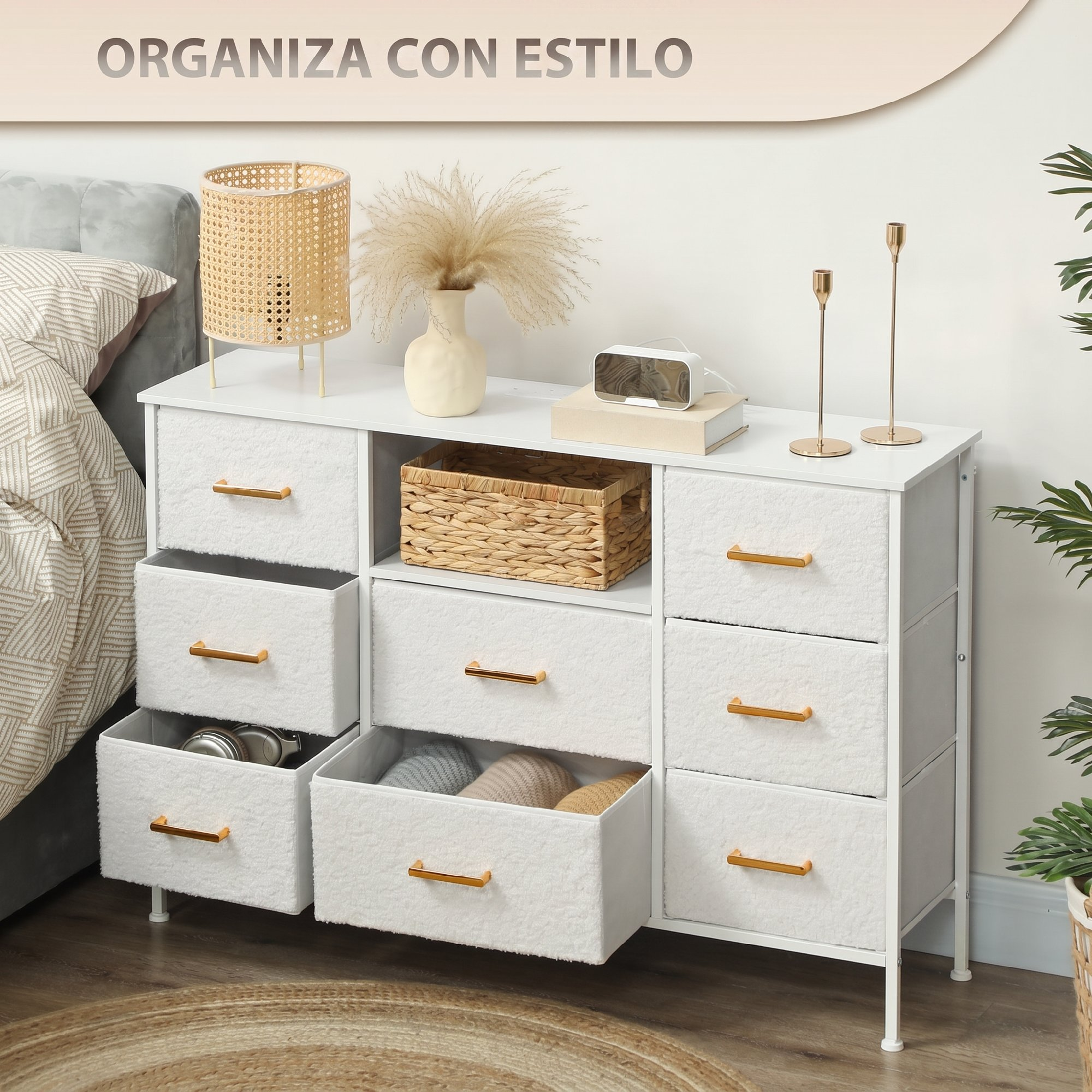 Una cómoda blanca con cajones de tela, tiradores dorados y decoración superior se encuentra en un dormitorio.