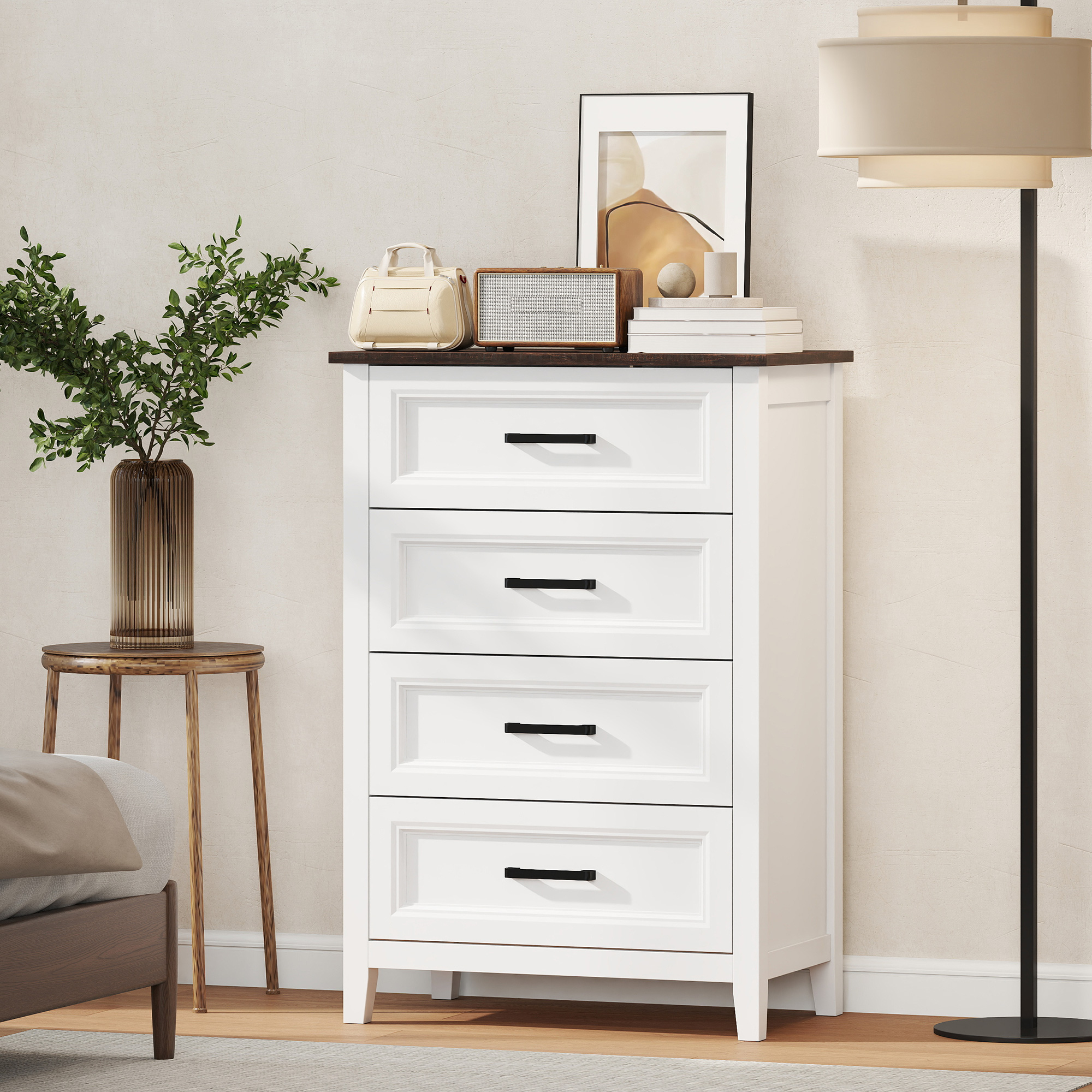 Una cómoda blanca con cuatro cajones se encuentra junto a una lámpara de pie y una mesa de madera con una planta.