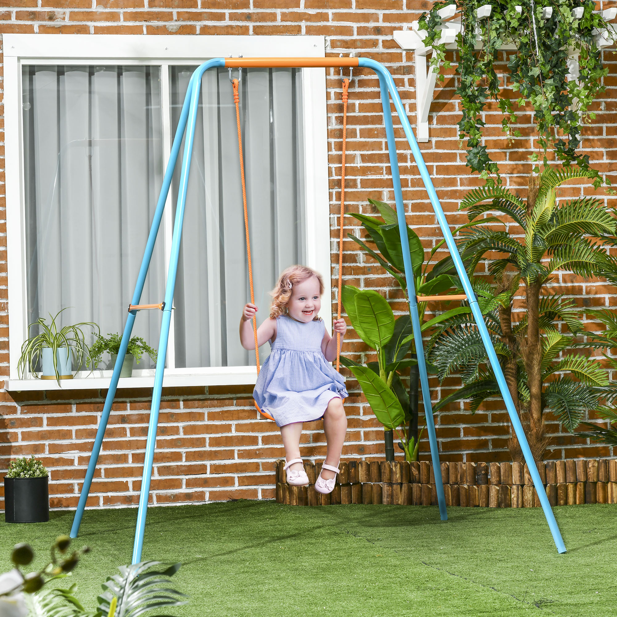 Bambina con capelli rosa e vestito blu dondola su un'altalena blu davanti a un muro di mattoni.