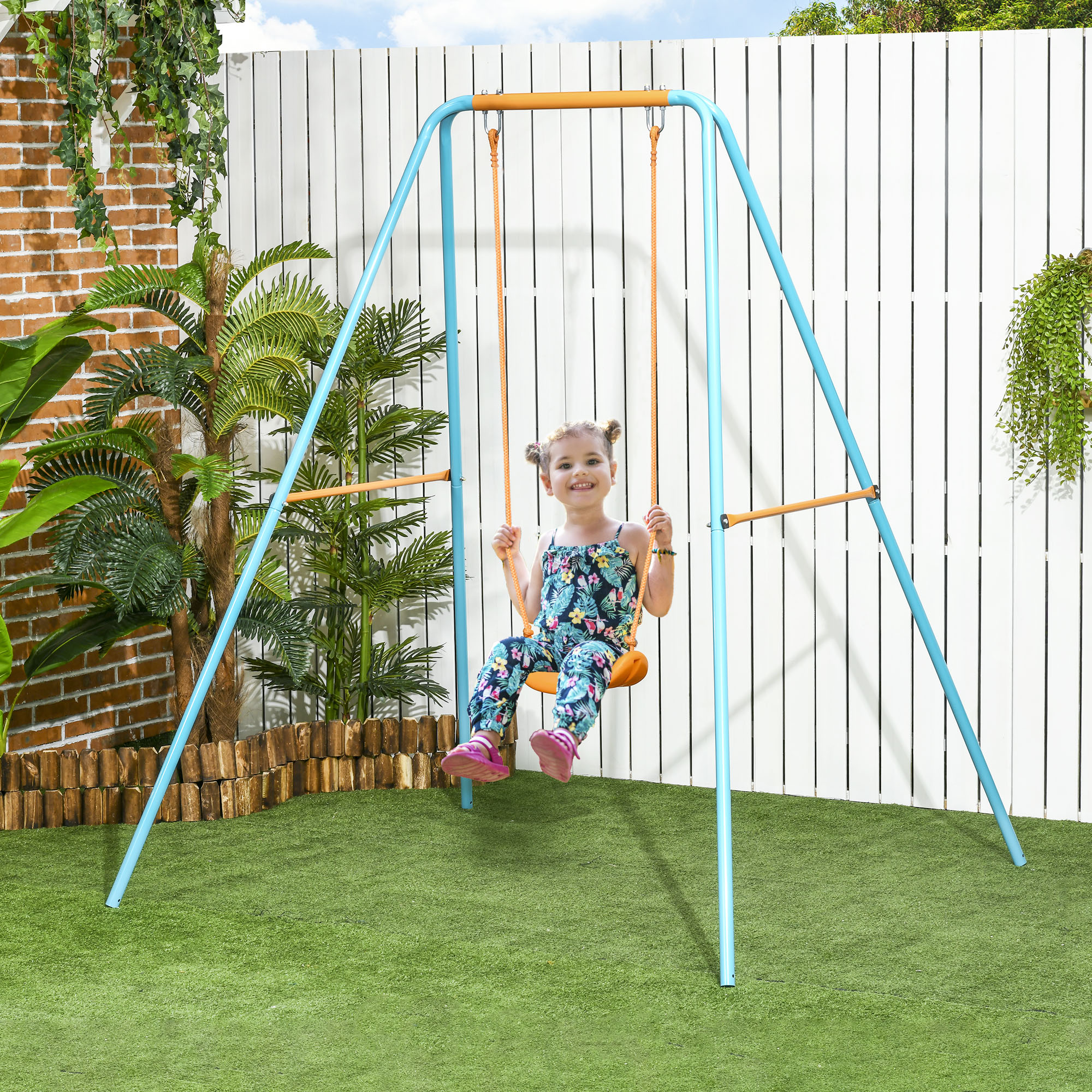 Una bambina con un abito colorato dondola su un'altalena blu in giardino.