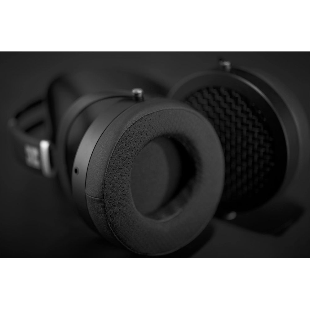 Primer plano de auriculares negros con almohadillas afelpadas y copas de malla texturizada sobre fondo oscuro.