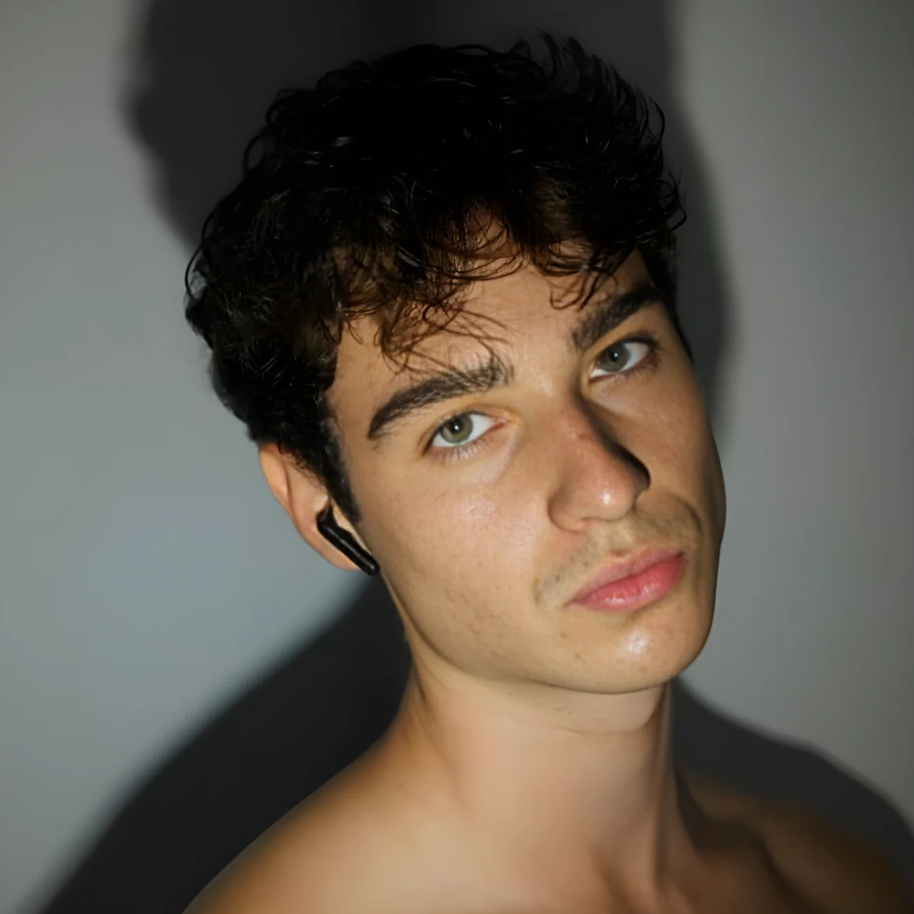 Retrato de un joven con cabello castaño rizado y ojos verdes frente a una pared brillante con su sombra.