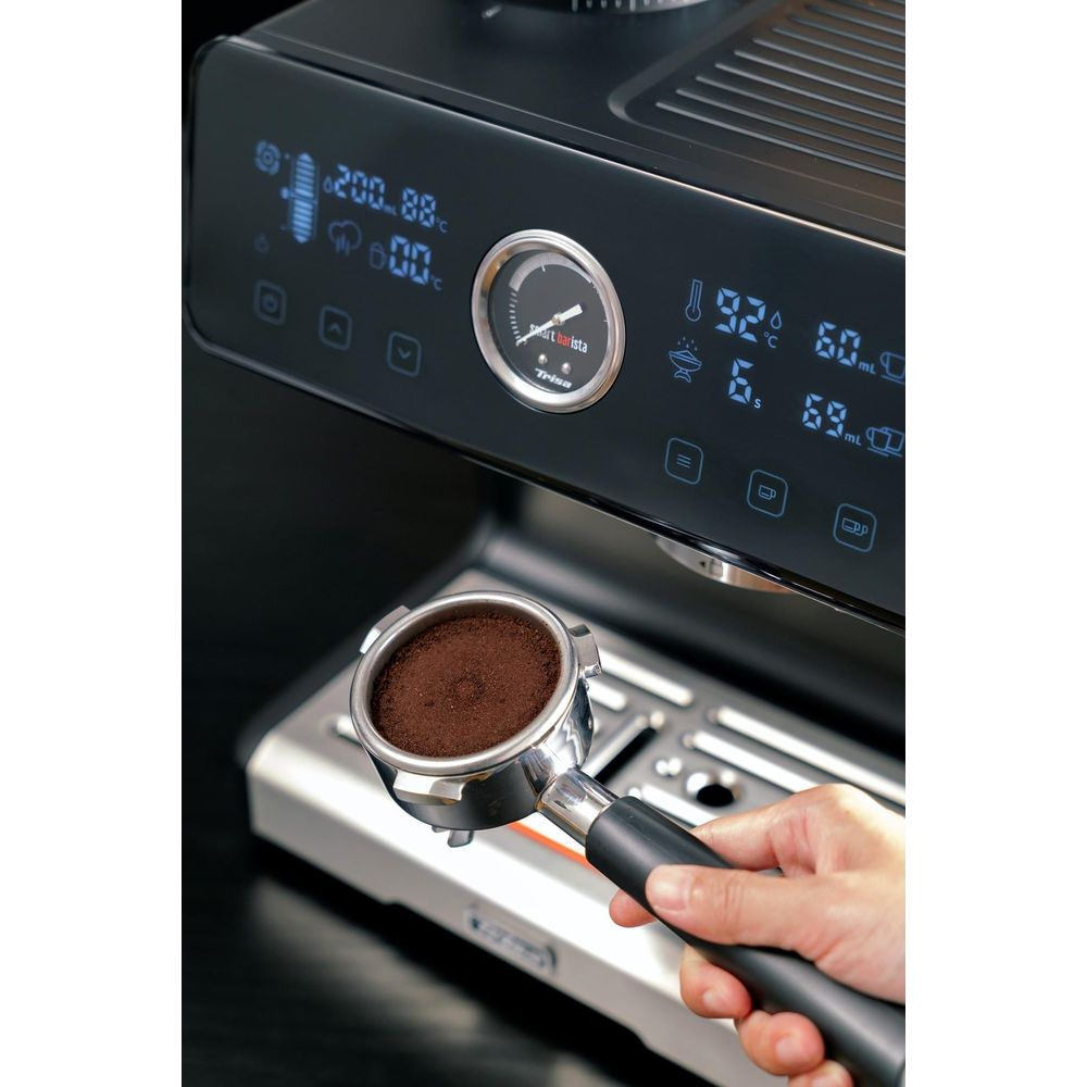 Una mano tiene un portafiltro pieno di caffè macinato davanti a una moderna macchina da caffè.