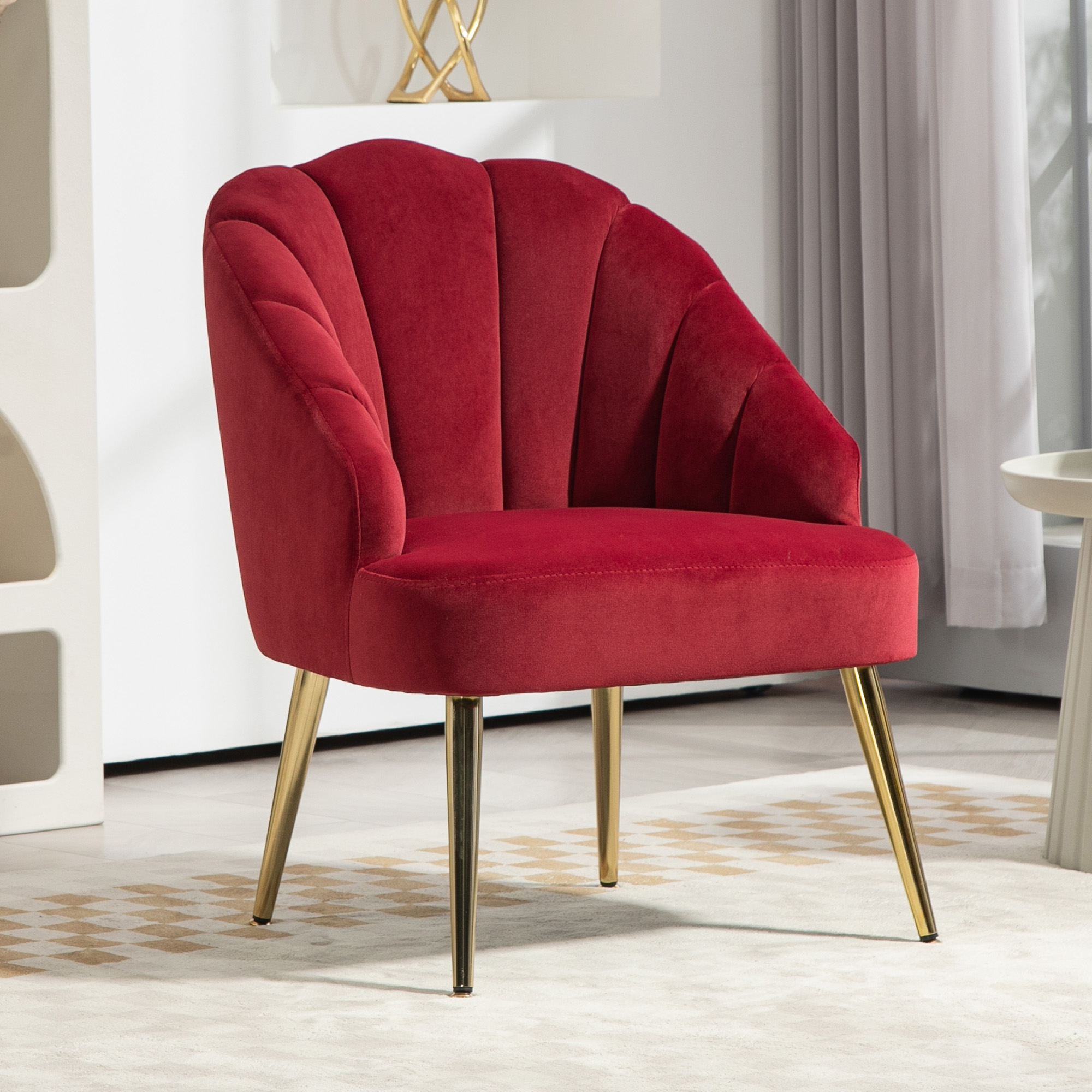 Poltrona in velluto rosso con design a conchiglia e gambe dorate su un tappeto.