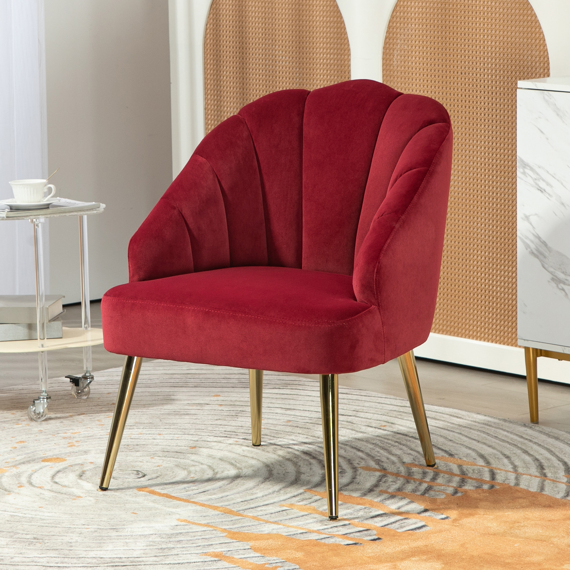 Poltrona in velluto rosso con design a conchiglia e gambe dorate su un tappeto fantasia.
