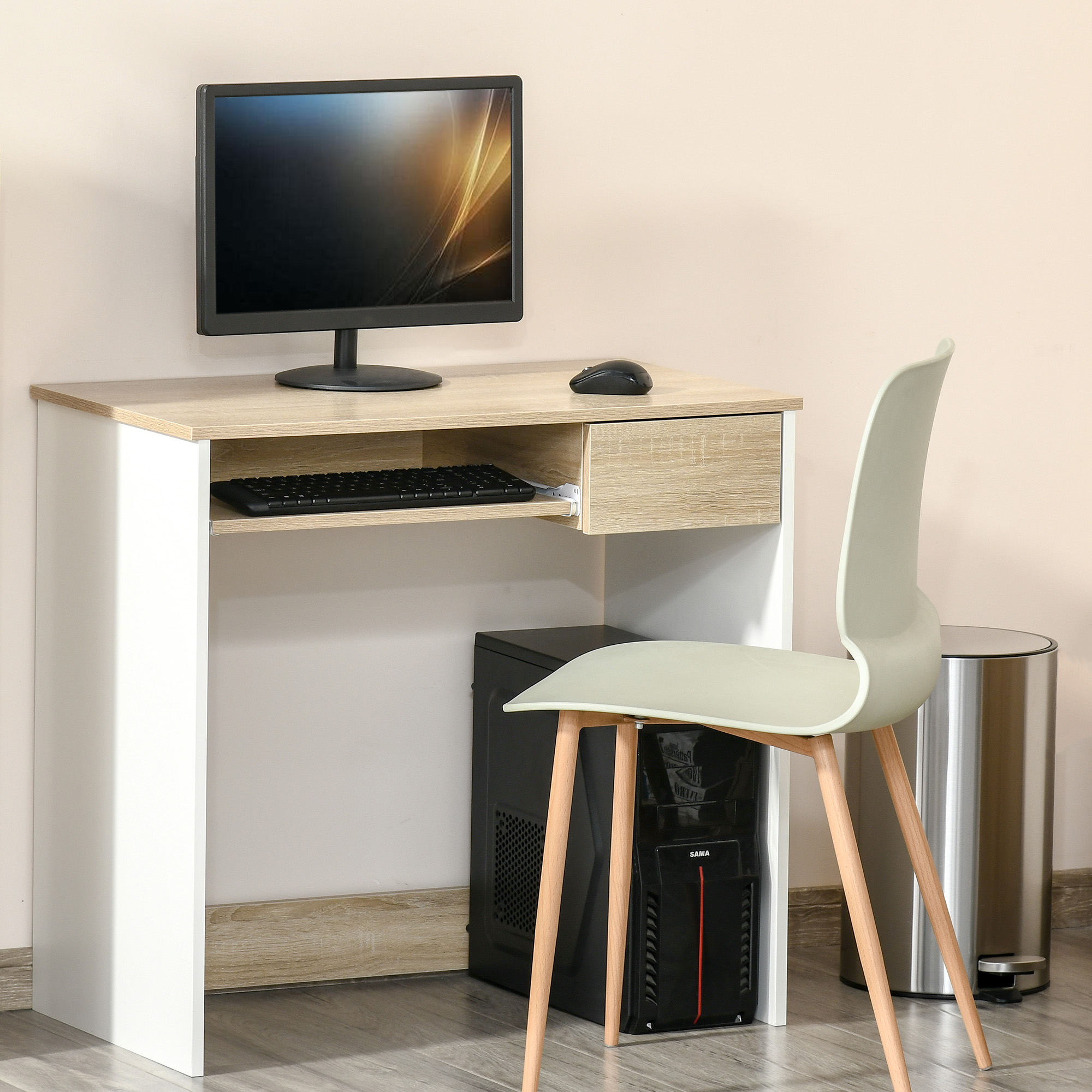 Una scrivania in legno chiaro con monitor, tastiera e mouse. Un computer sotto e una sedia verde chiaro davanti.