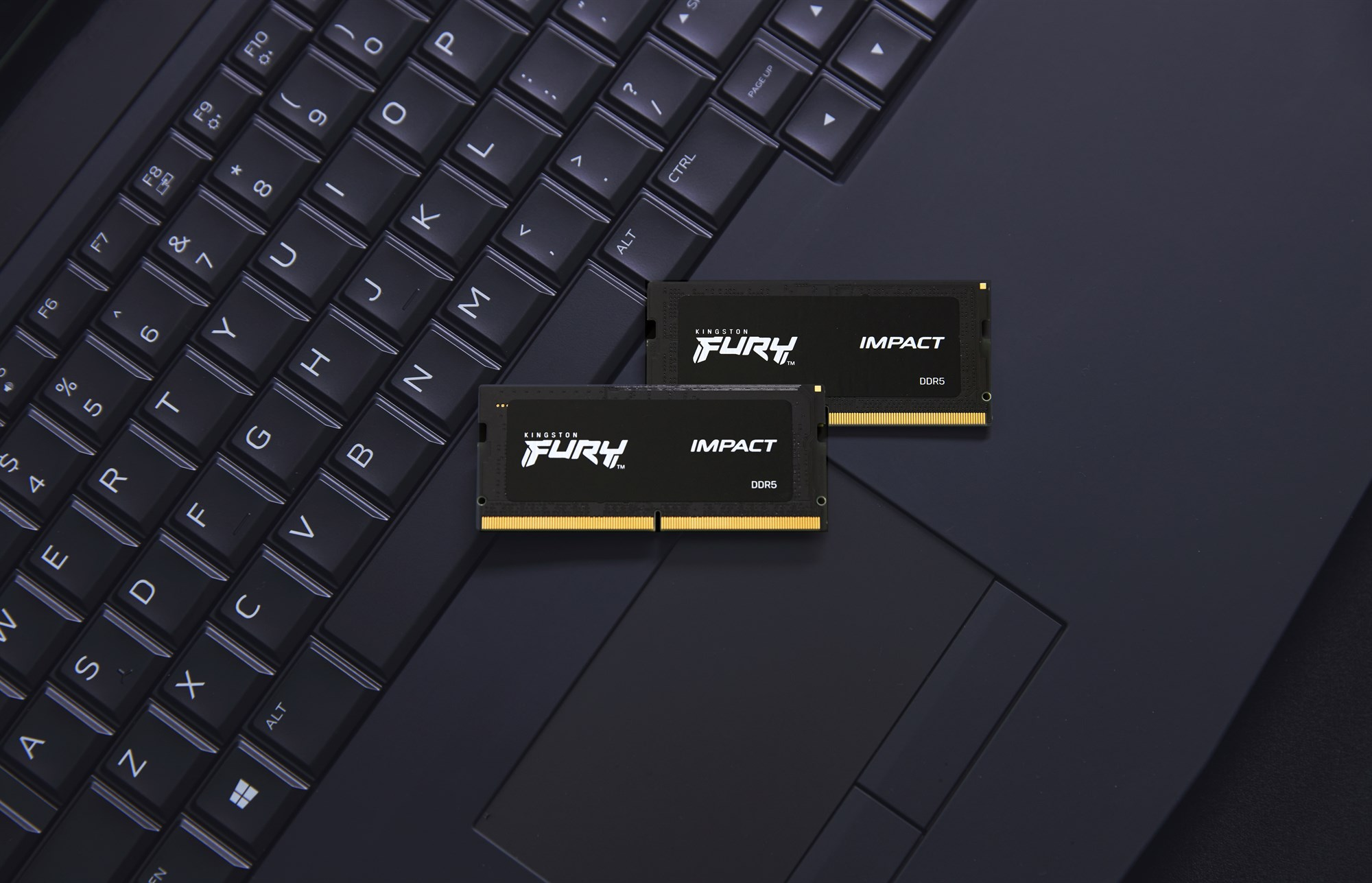 Due moduli RAM Kingston Fury Impact DDR5 poggiano sulla tastiera di un computer portatile nero.