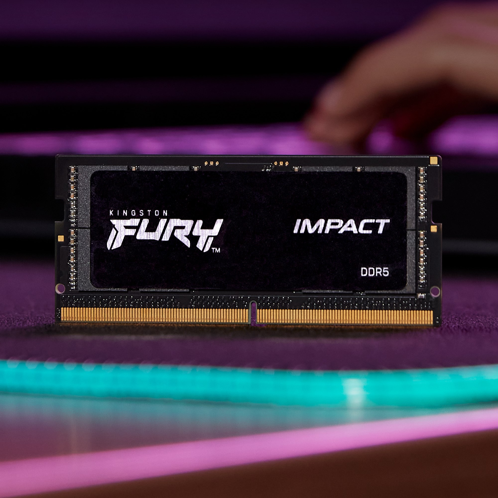 Modulo RAM Kingston Fury Impact DDR5 su un tavolo scuro con illuminazione rosa e sfondo sfocato.
